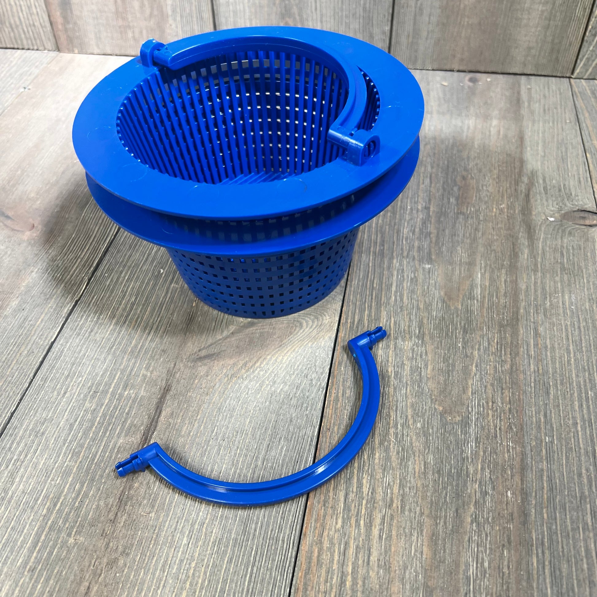 Alt text: Blue pool skimmer basket with a detachable handle on a wooden surface.