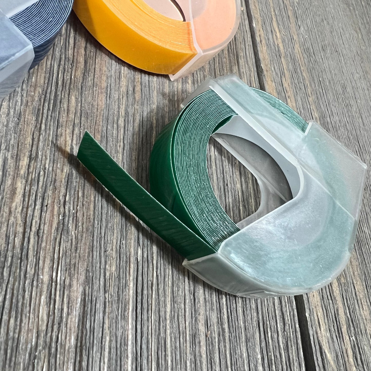 Embossing label tape for Dymo label makers in yellow, green, and blue on a wooden surface.