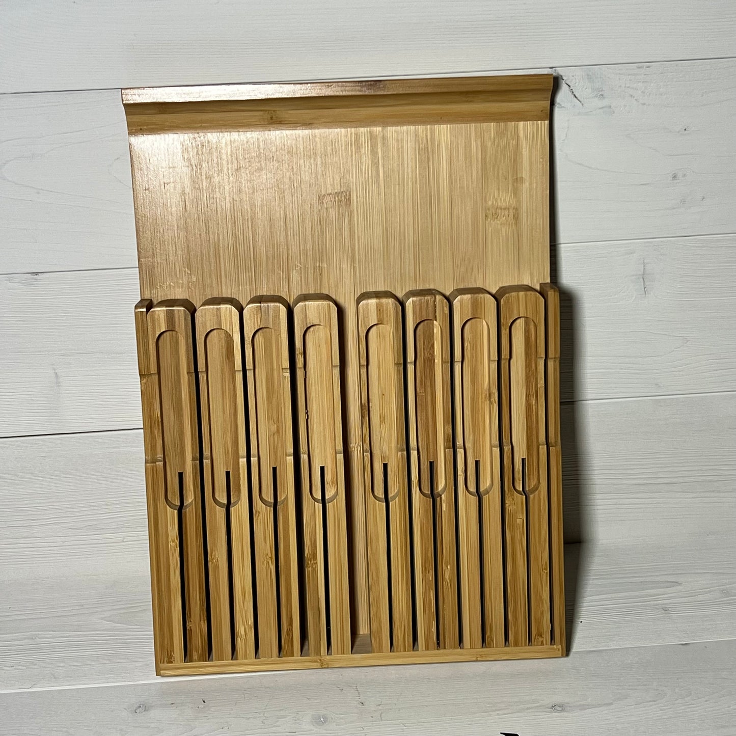 Alt text: Bamboo in-drawer knife block organizer for 16 knives and a sharpener on a light wood background.
