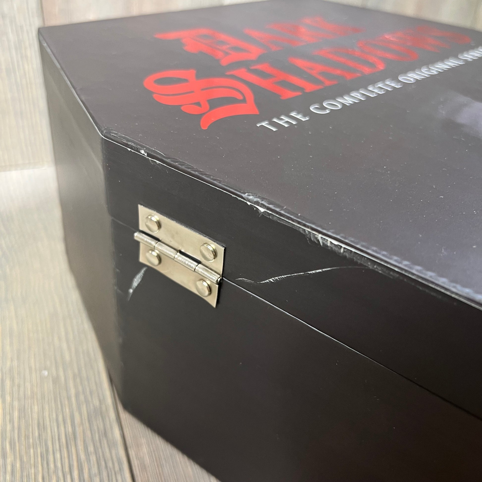 Cracked corner of a Dark Shadows DVD box set with visible hinge on a wooden surface.