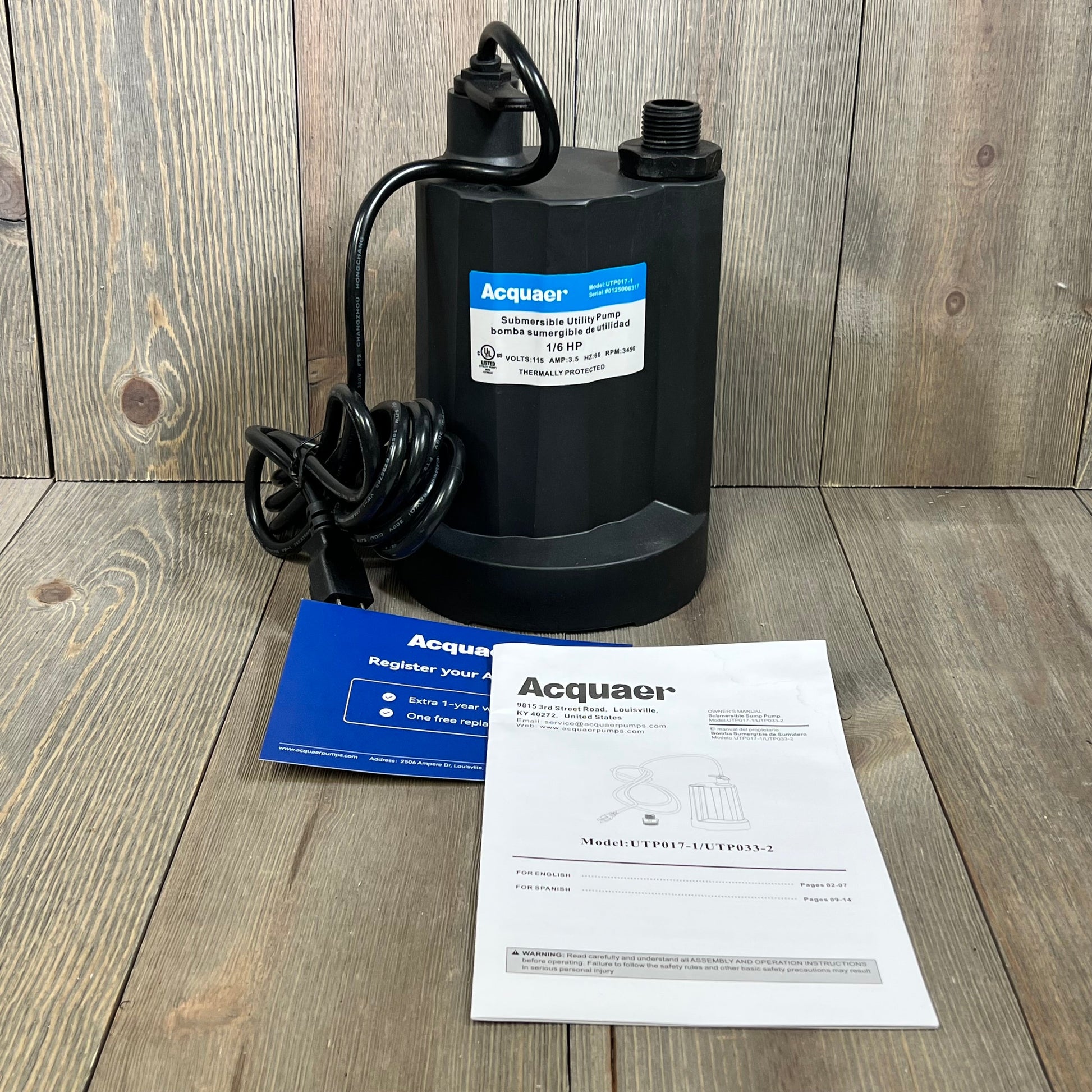 Acquaer submersible sump pump with cord, instruction manuals, and registration card on wooden floor.