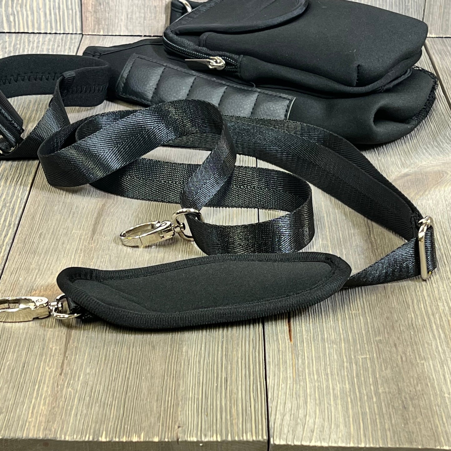 Black detachable shoulder strap of magnetic water bottle carrier bag on wooden surface.