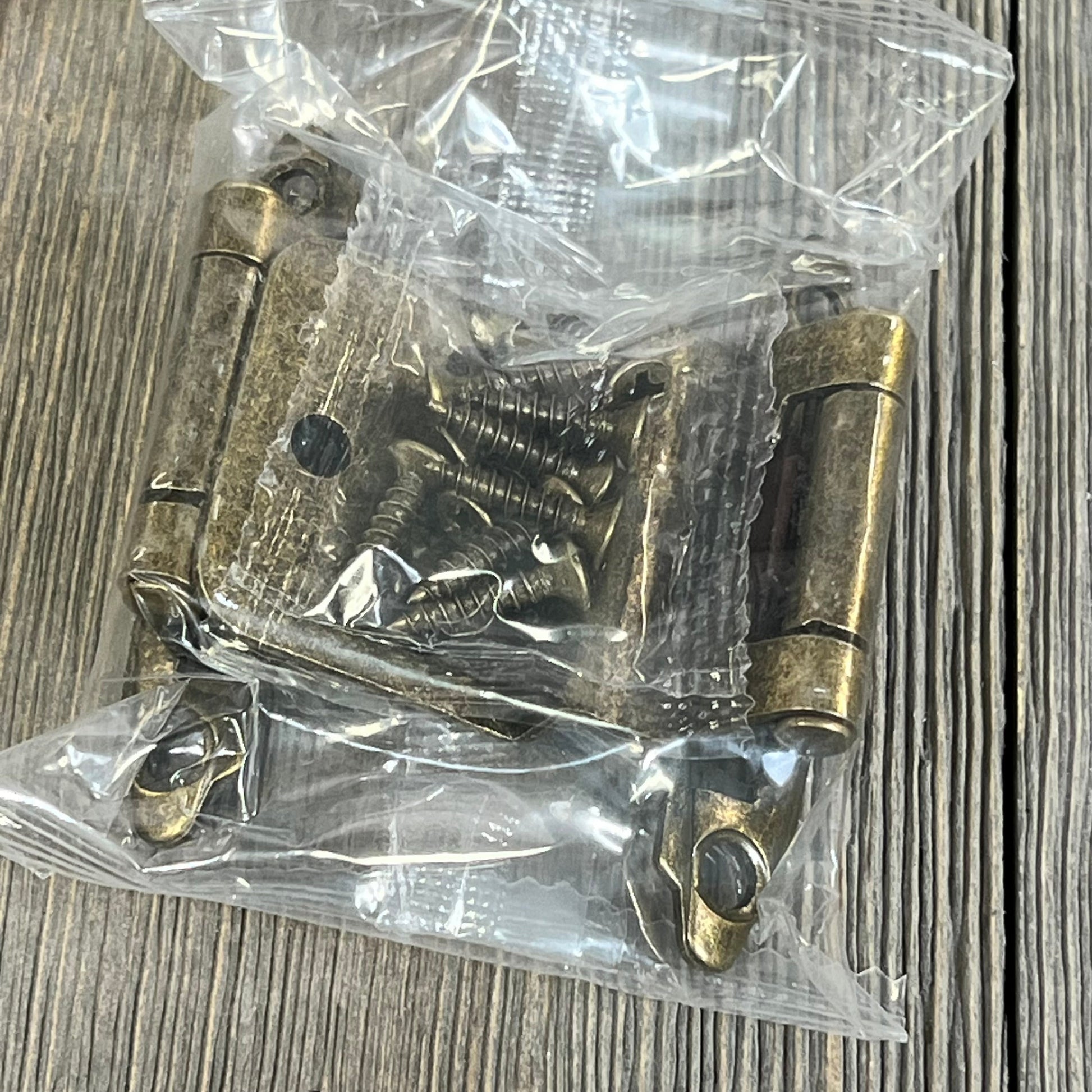 Antique brass inset cabinet door hinges with screws, packaged on wood background, ideal for kitchen cabinets.