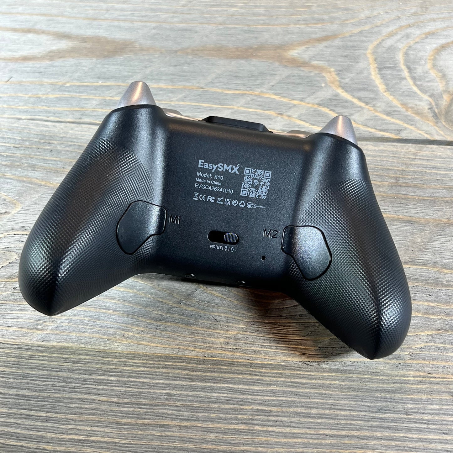 Back view of EasySMX X10 Wireless Bluetooth Controller showcasing textured grips on a wooden surface.