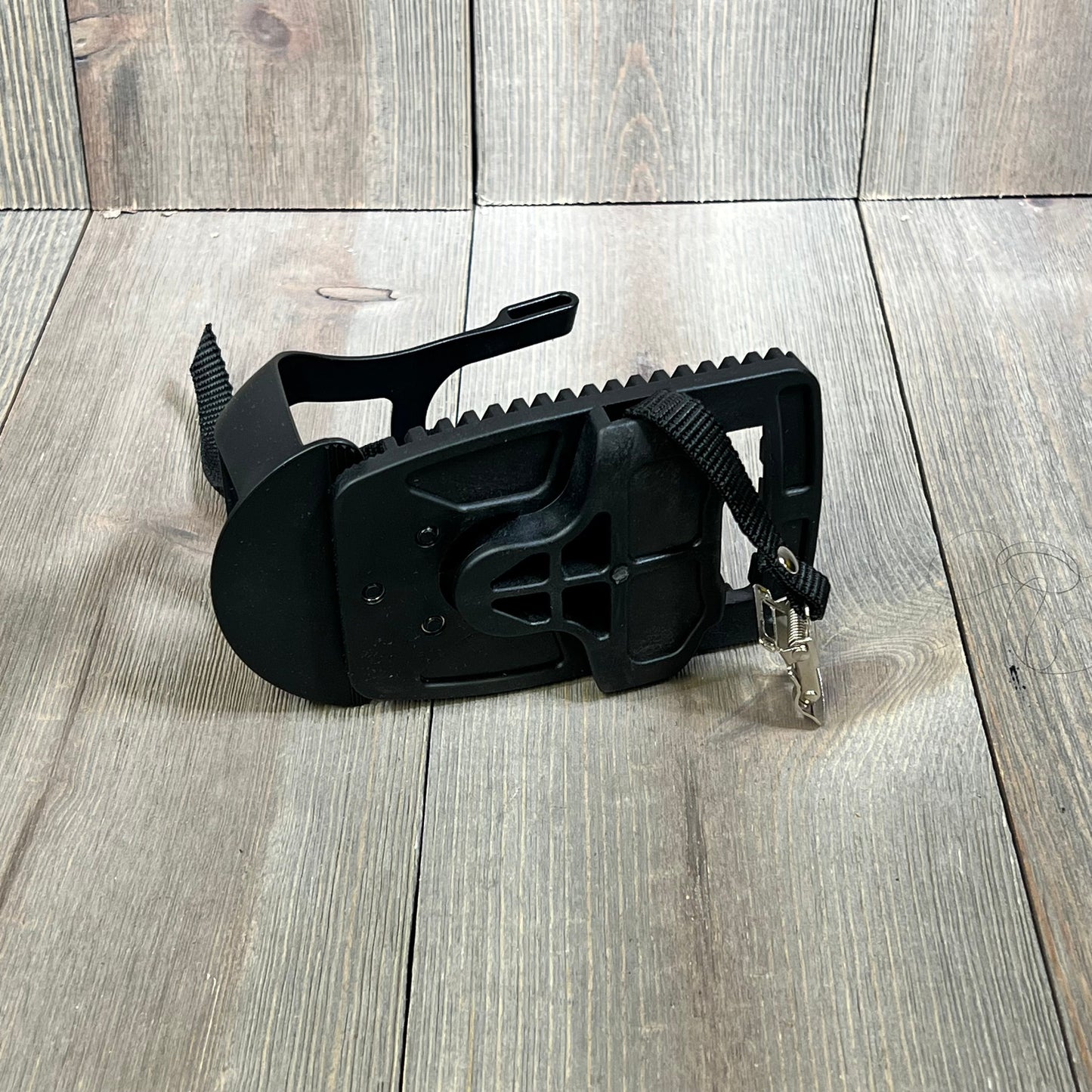 Black Kelecuia toe cage pedal adapter for Peloton bike, featuring adjustable straps for secure sneaker fit on wooden floor.