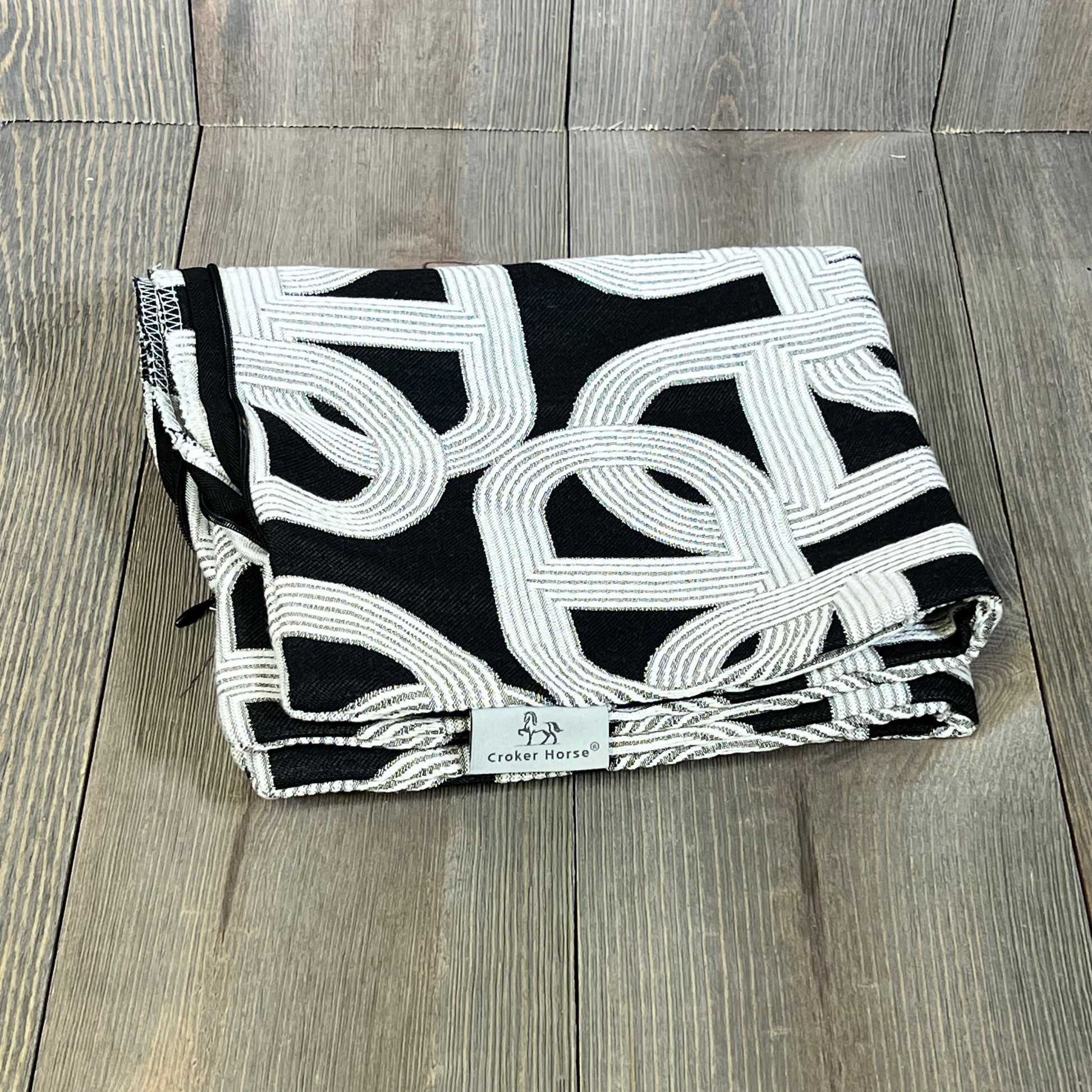 Luxury Croker Horse throw pillow cover with black embroidery, folded on wooden floor, modern pig nose horseshoe design.