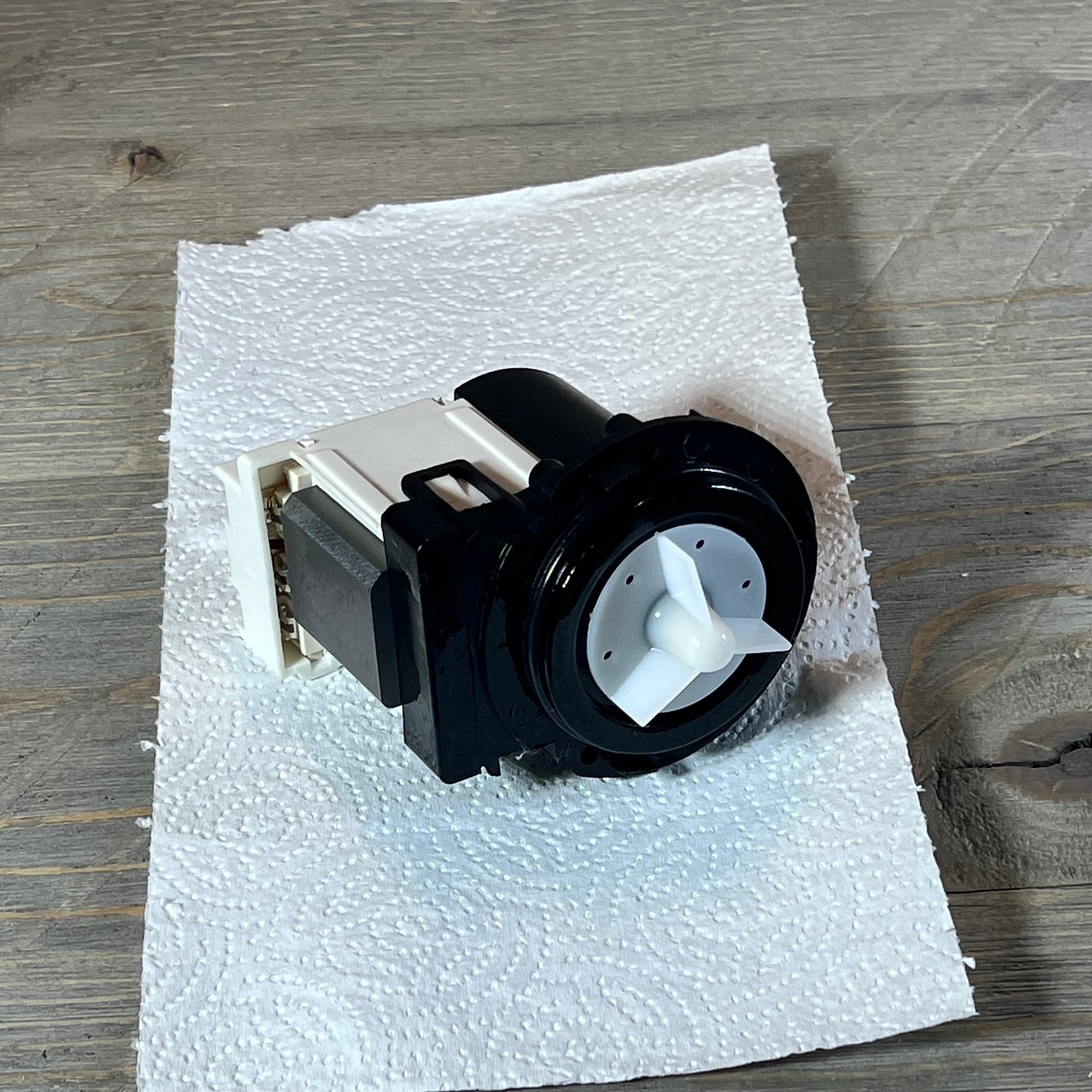 Black and white washer drain pump motor for Kenmore and LG, replacing model 4681EA2001T, placed on a paper towel.