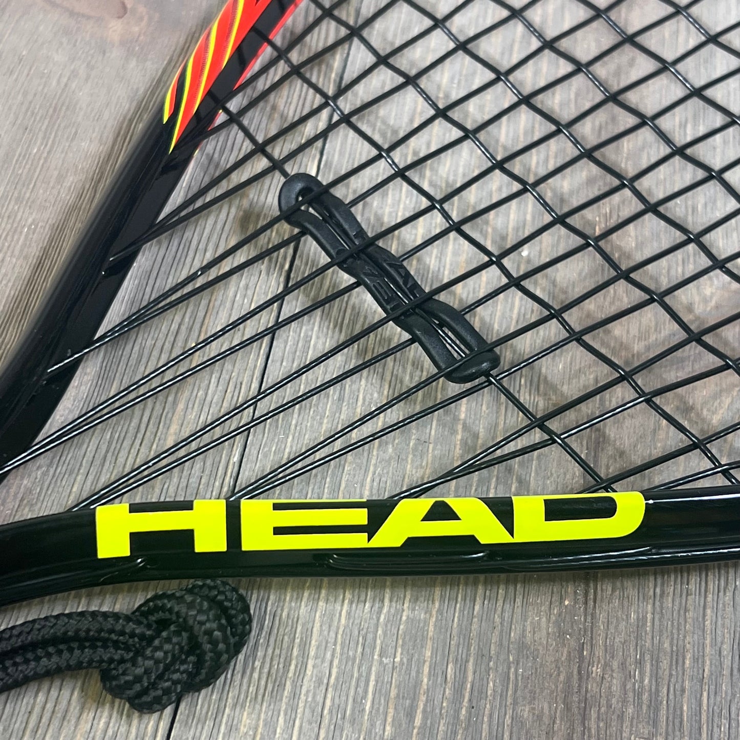 Close-up of HEAD CPS Heat Racquetball Racquet strings and frame, showcasing durable construction and vibrant logo design.