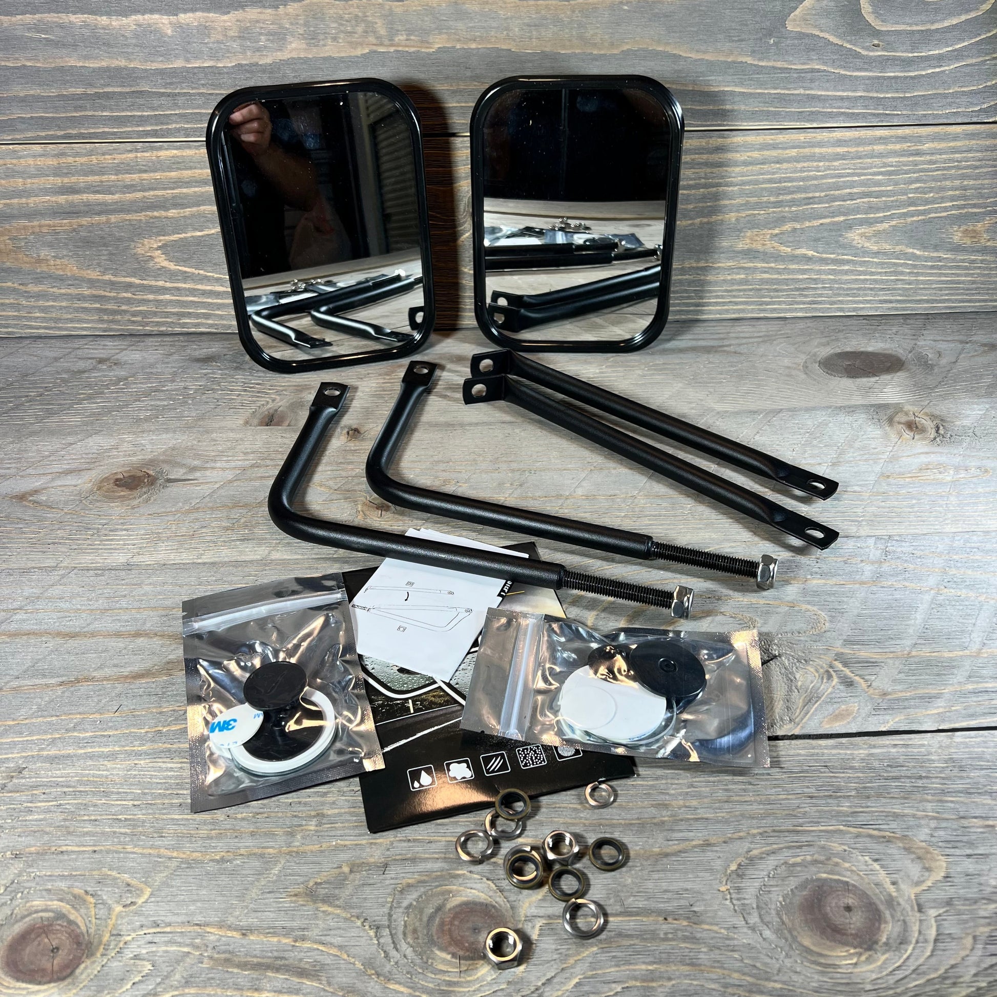 Black anti-shake mirrors for Jeep Wrangler with mounting hardware on a wooden surface.