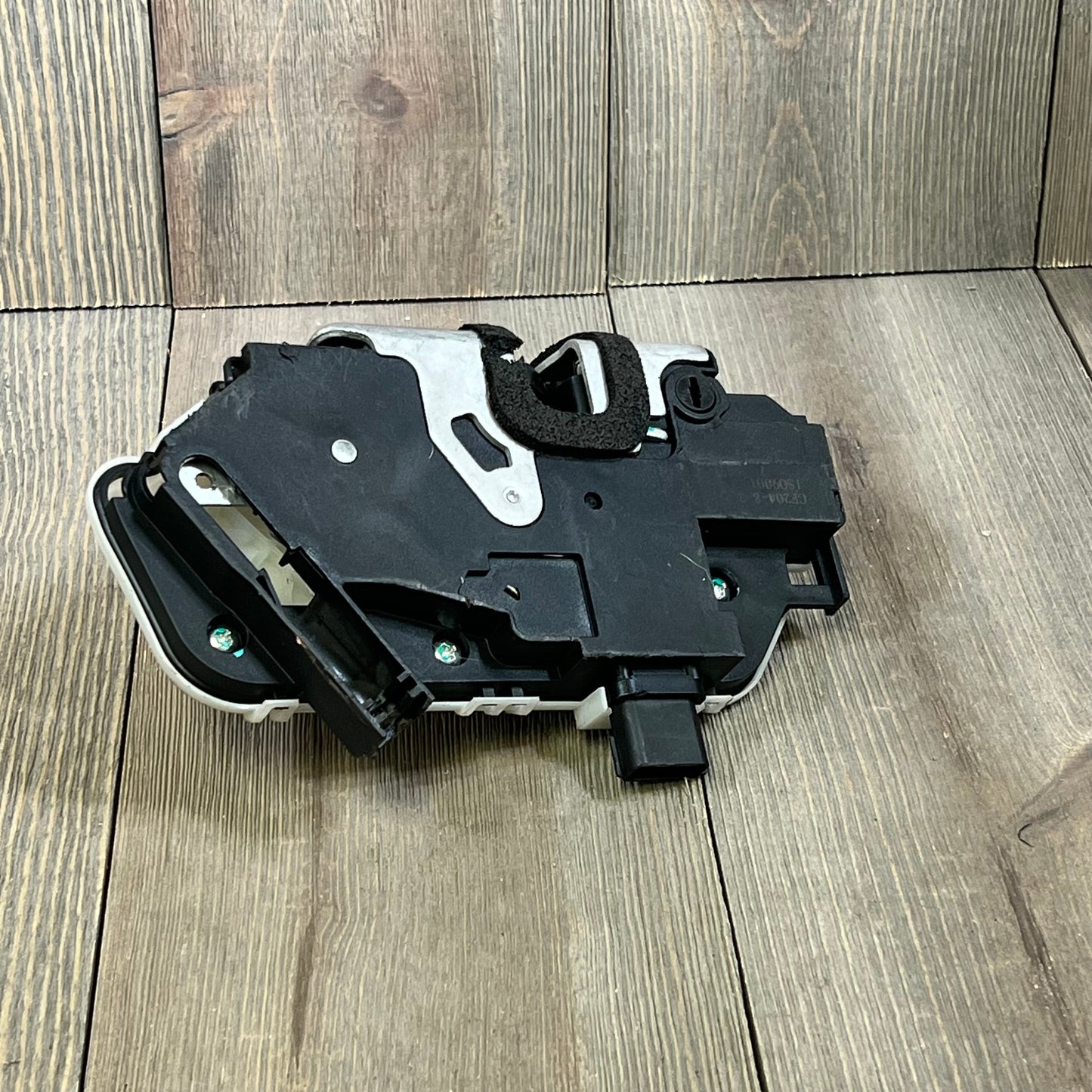 REVOTUNE rear left door latch lock actuator for Ford F-150 and Lincoln, black and silver components on wood surface.