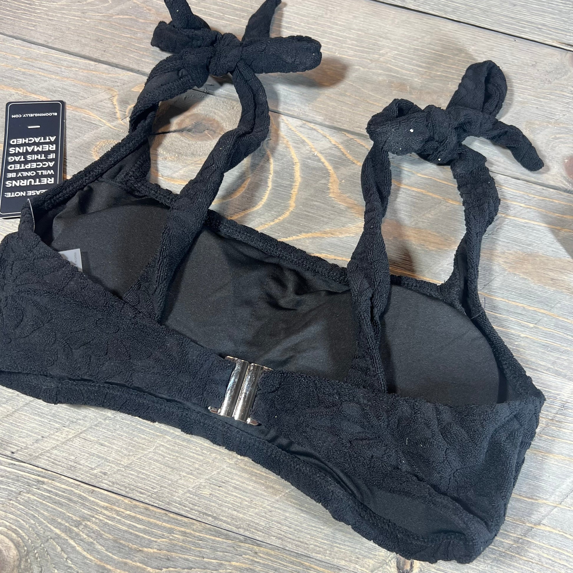 Black bikini top with adjustable tie straps and a secure back clasp, showcasing intricate fabric detailing.