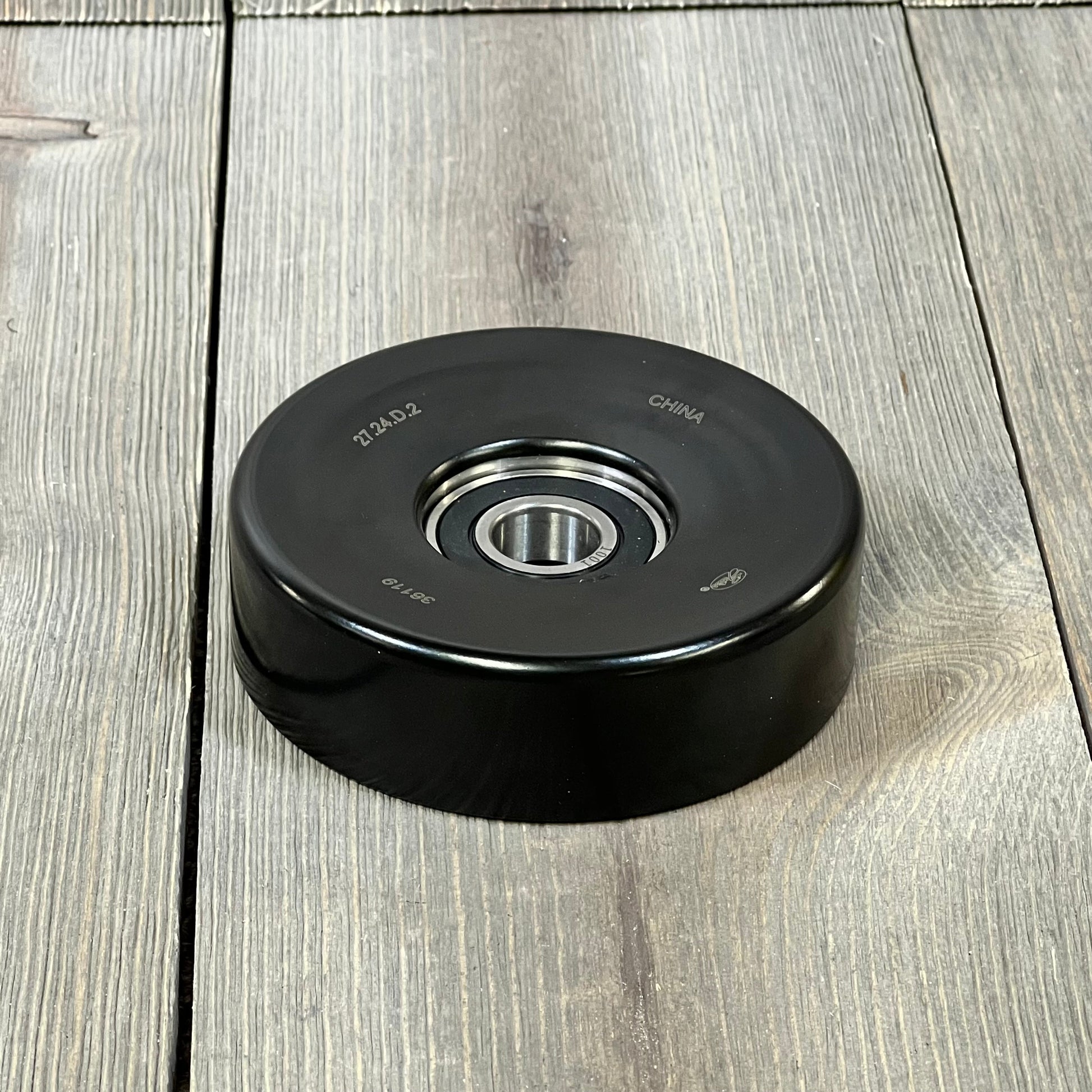 ACDelco Gold 36119 Idler Pulley on wooden surface, showcasing durable black construction and precision bearing.