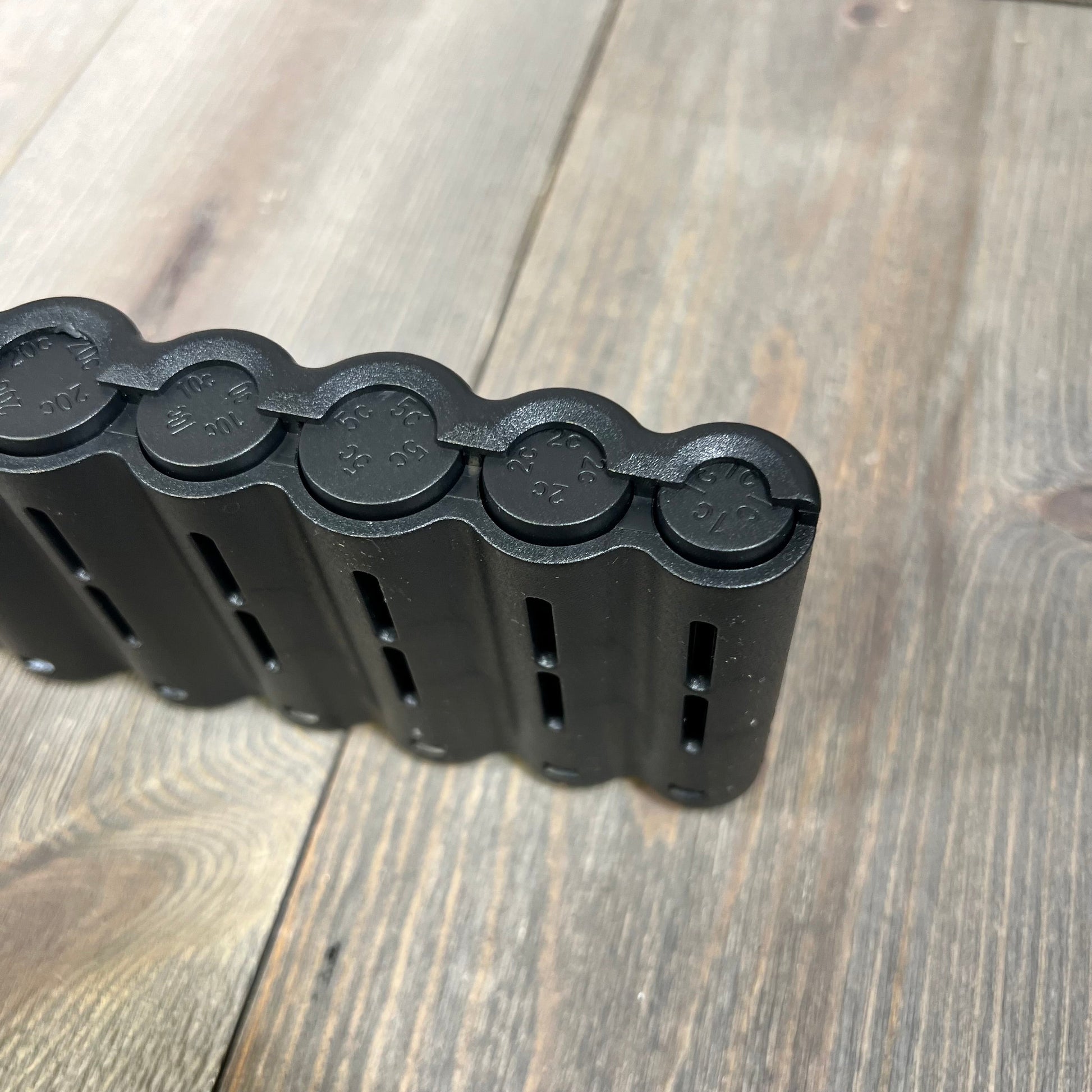 Black coin holder with slots for euro coins, featuring a sleek design on a wooden surface. Ideal for organized storage.