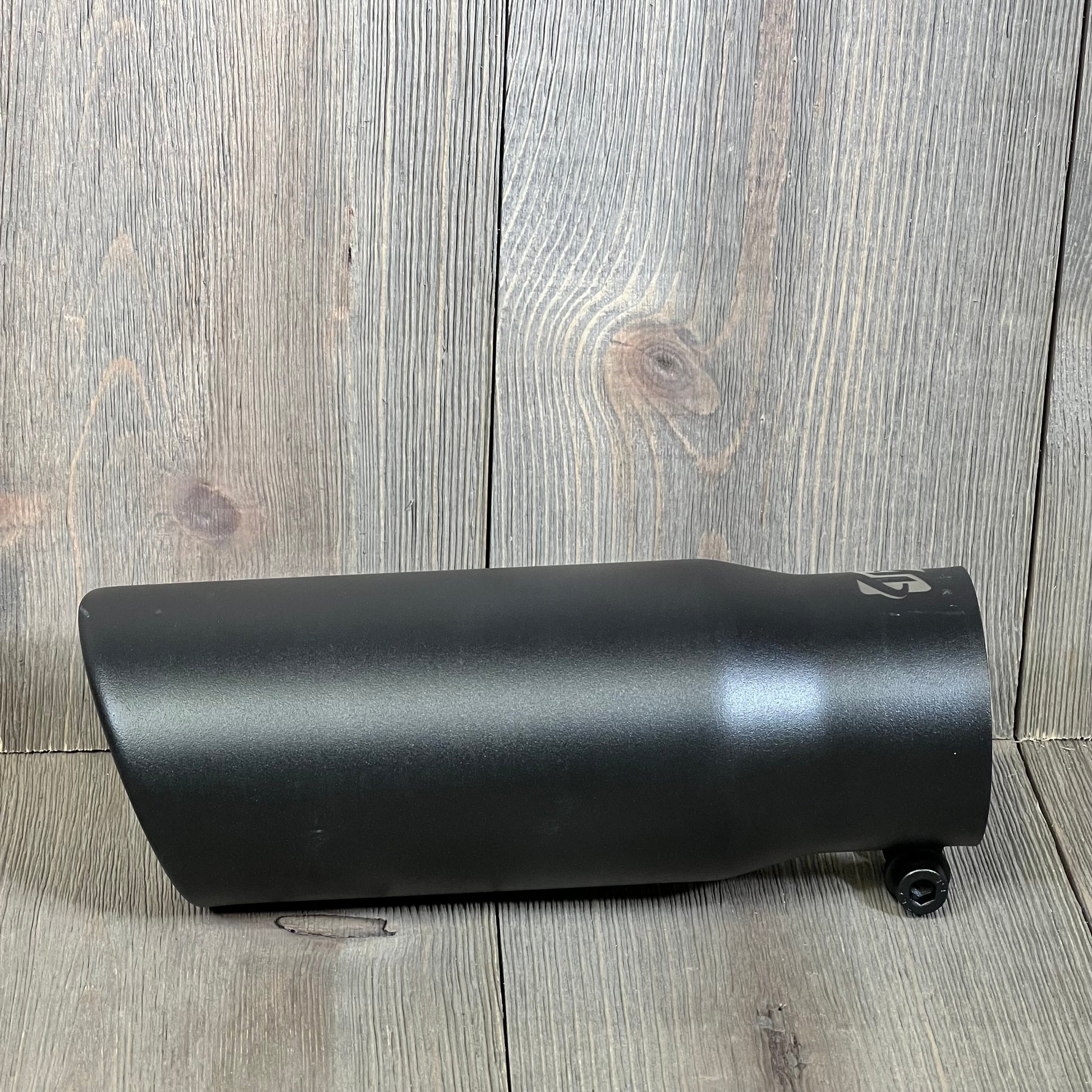 Black coated stainless steel exhaust tip, 2.5" inlet, 3" outlet, bolt-on design, shown on wooden surface.