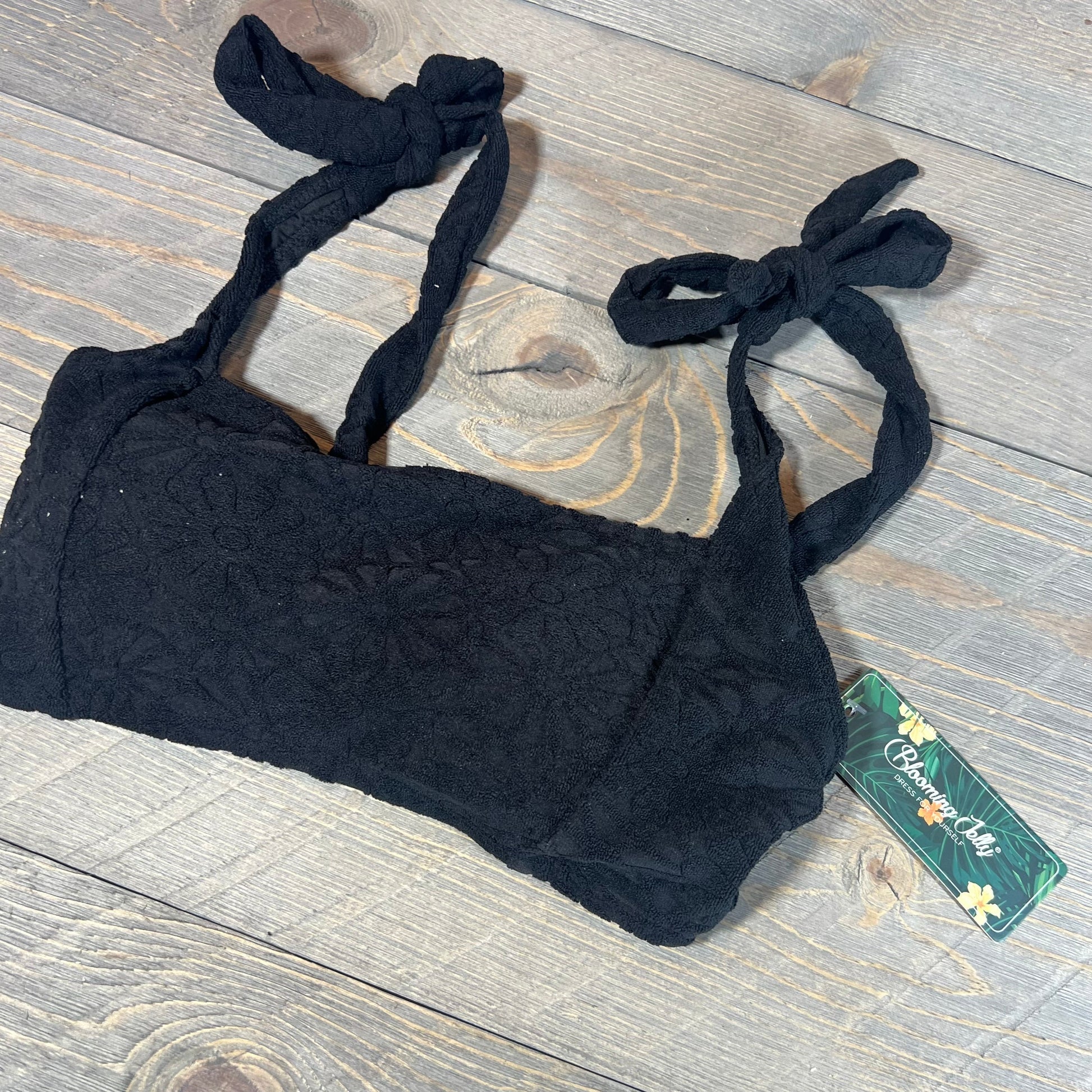 Black high-waisted bikini top with floral texture and tie straps on a wooden surface.