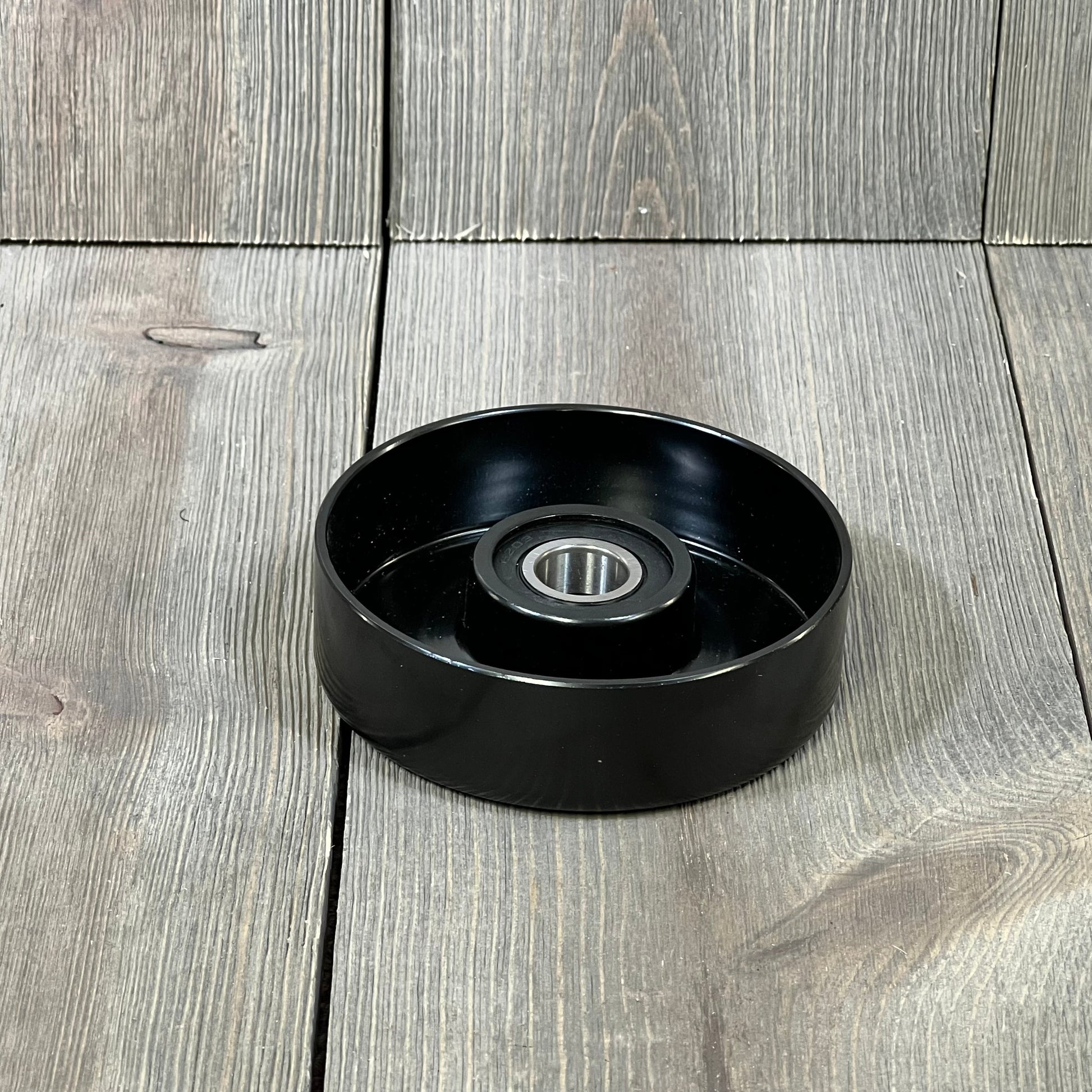 Black ACDelco Gold 36119 Idler Pulley on wooden surface, showcasing smooth design and durable construction.