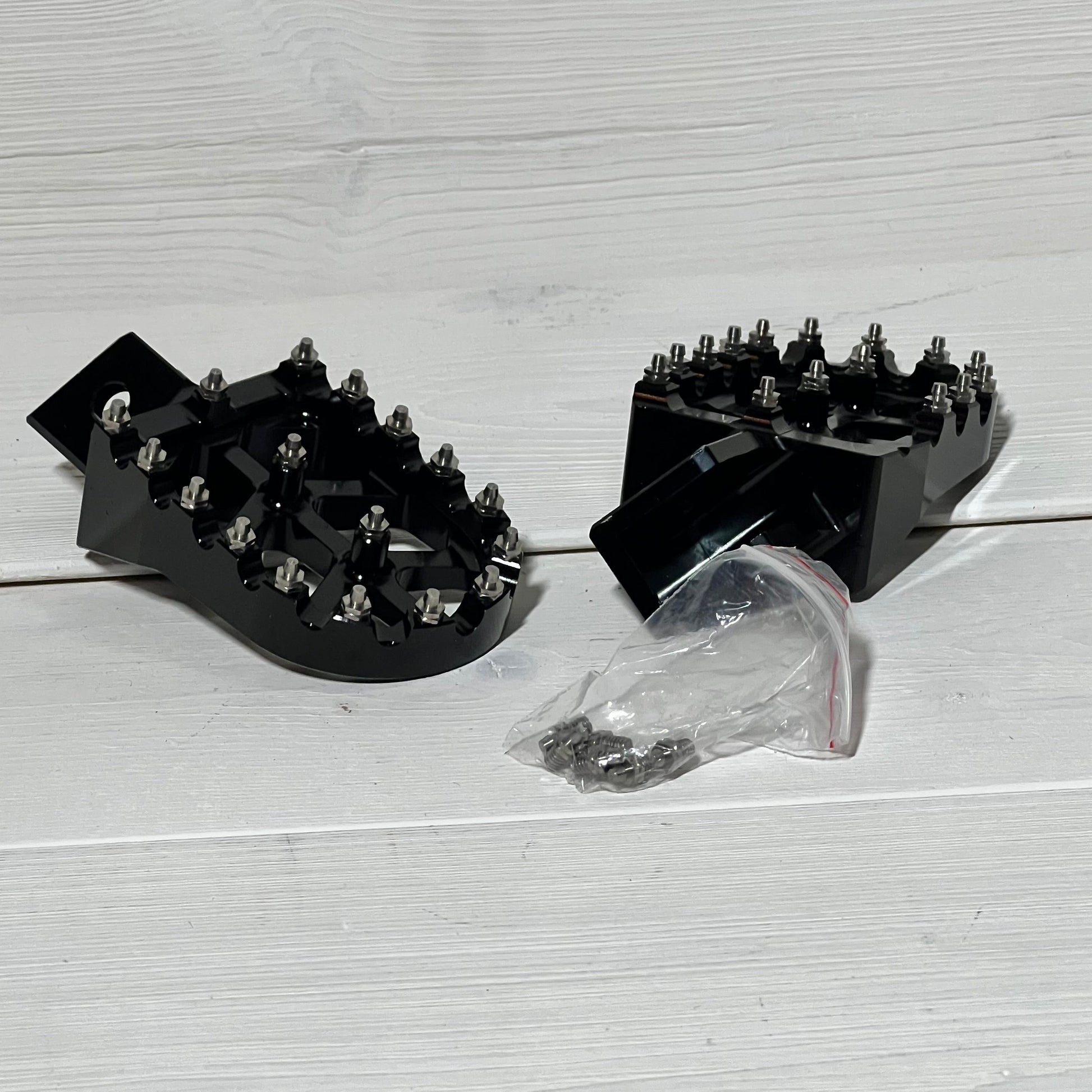 Black AnXin motorcycle foot pegs for PW50 and PW80 dirt bikes, featuring a robust, spiked design with mounting hardware.