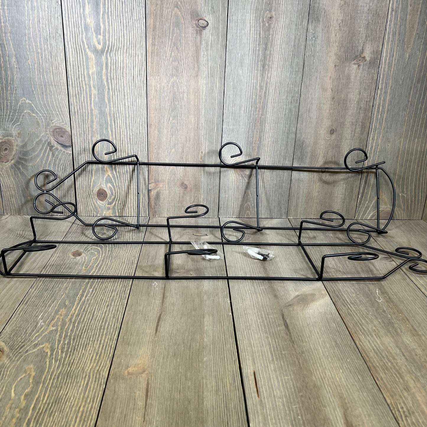Black 3-tier vertical wall plate holder with scroll design, perfect for displaying decorative dishes on wooden background.