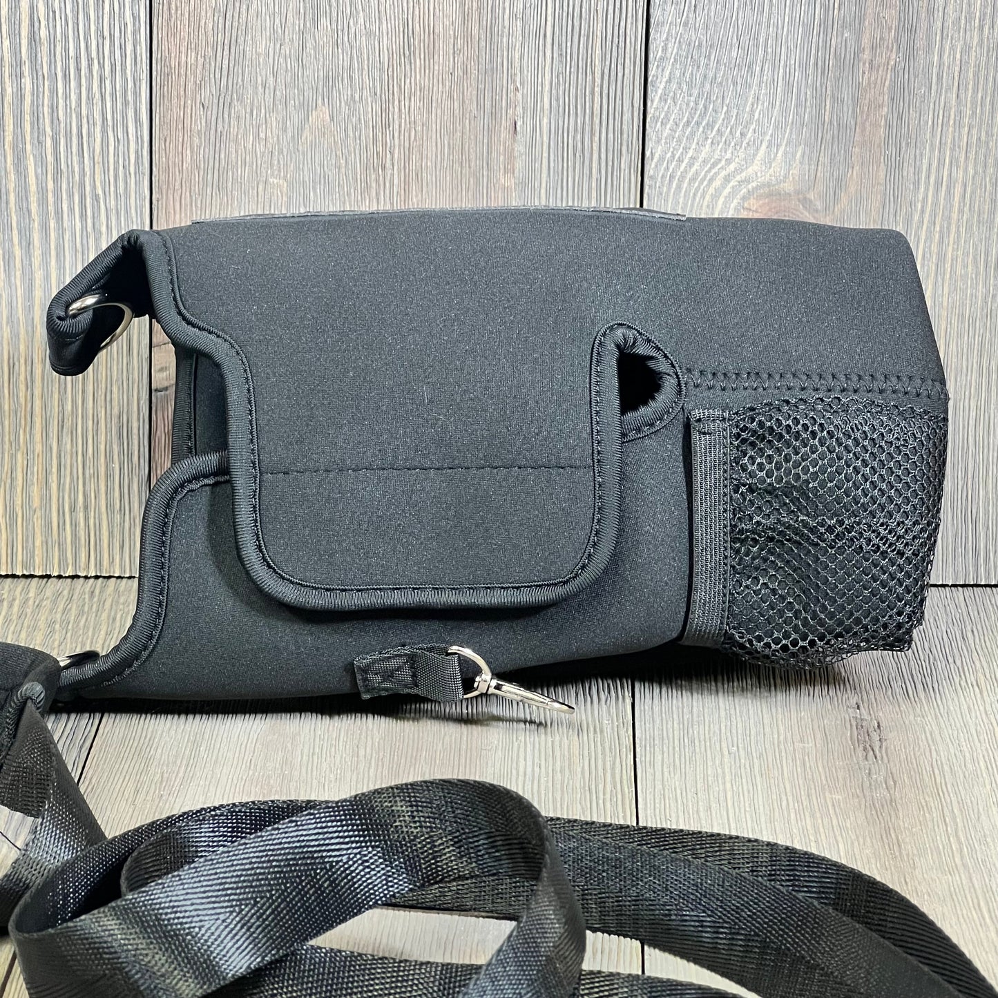 Black magnetic water bottle carrier bag with detachable shoulder strap and storage pouches on wooden background.