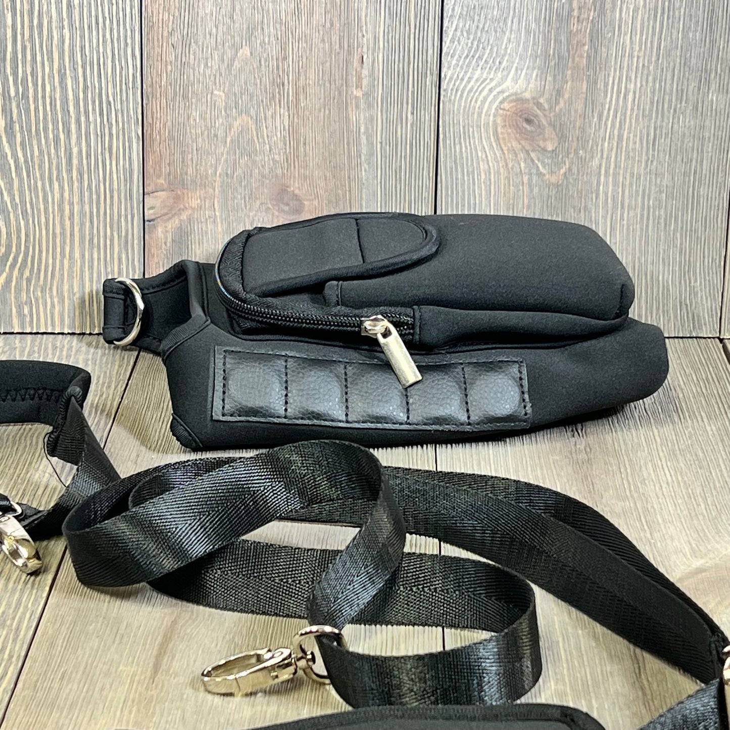 Black water bottle carrier bag with detachable strap, magnetic closure, and storage pouches on wood background.
