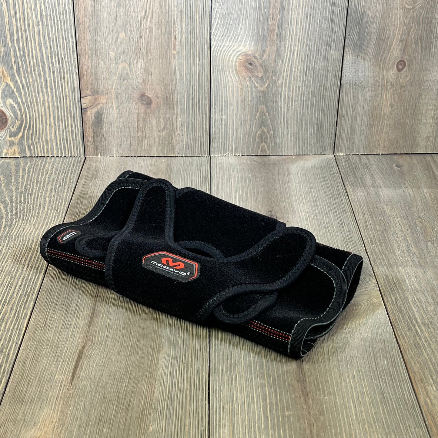 Black McDavid MD4201 knee wrap with stays, small size, offering versatile support and comfort on a wooden surface.