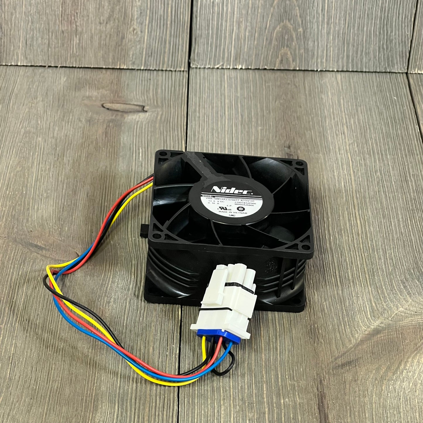 GE refrigerator evaporator fan motor WR60X26866 with colorful wires on wooden surface.