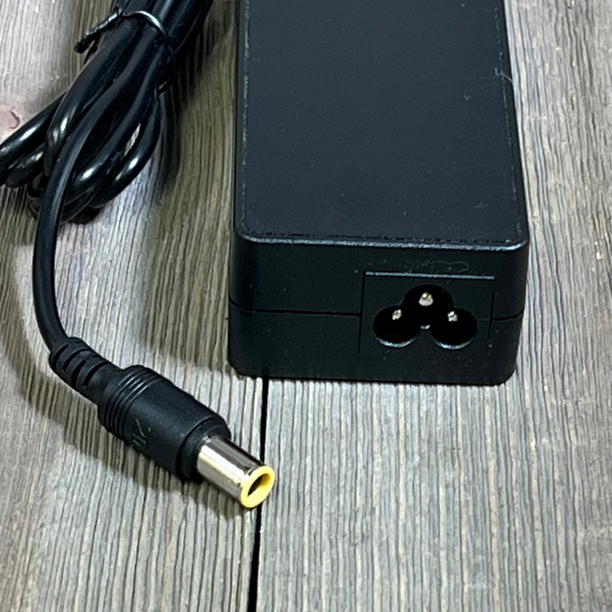 Black 24V 90W AC adapter for Jackery Explorer power stations, featuring a durable power cord and connector on a wooden surface.