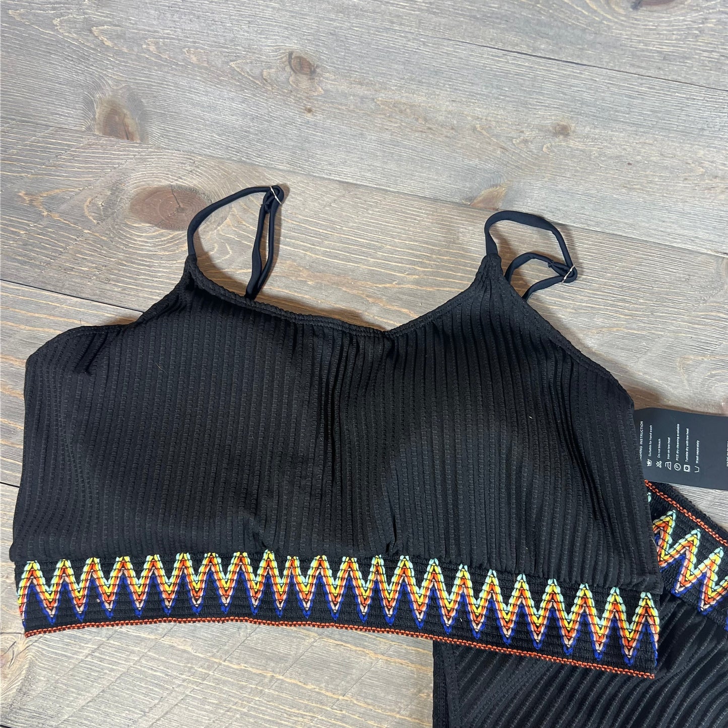 Black ribbed bikini top with colorful zigzag trim on a wooden background, part of the Lilosy set in XXL.
