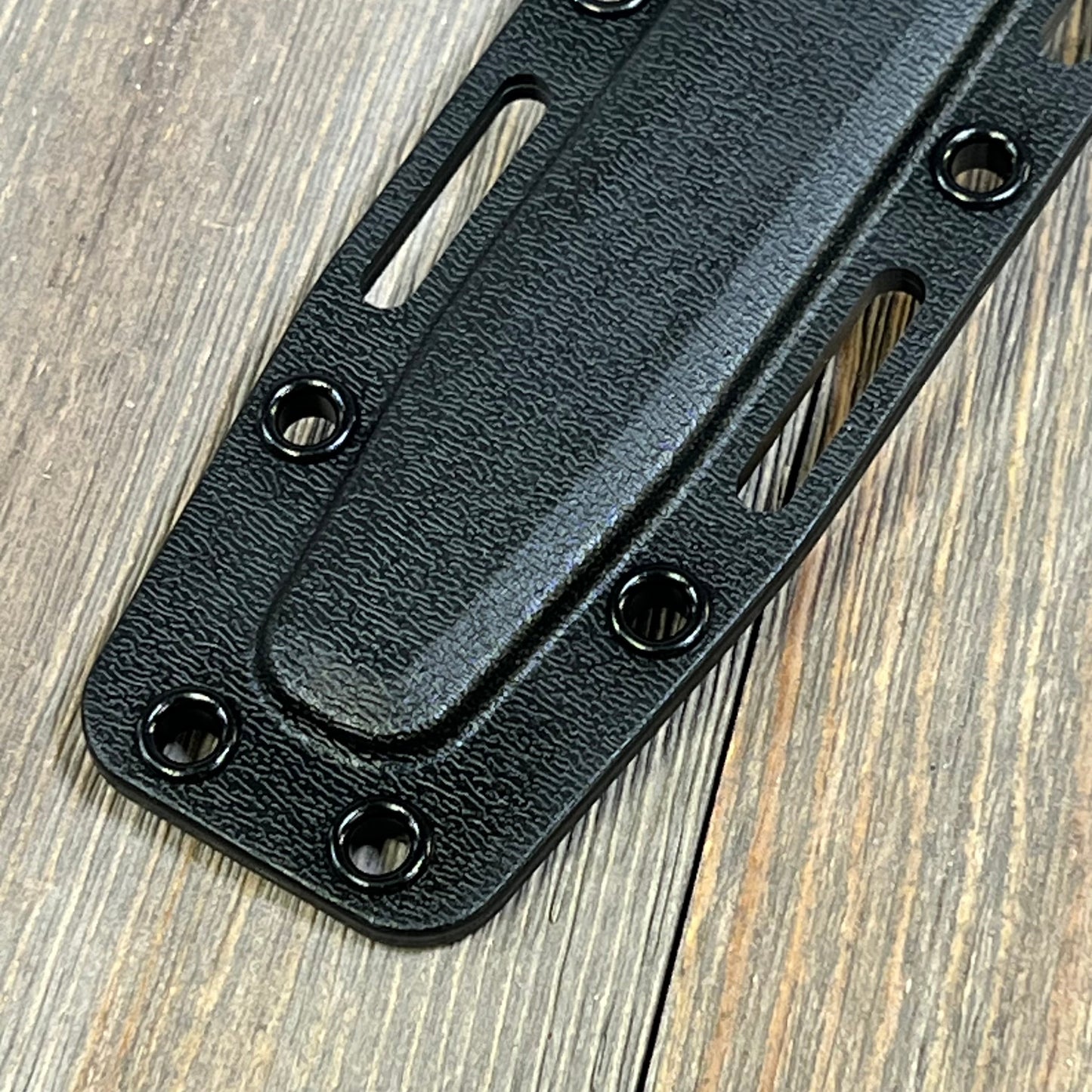 Black Ka-Bar Kydex sheath for short knives, featuring durable texture and multiple rivets on a rustic wooden surface.