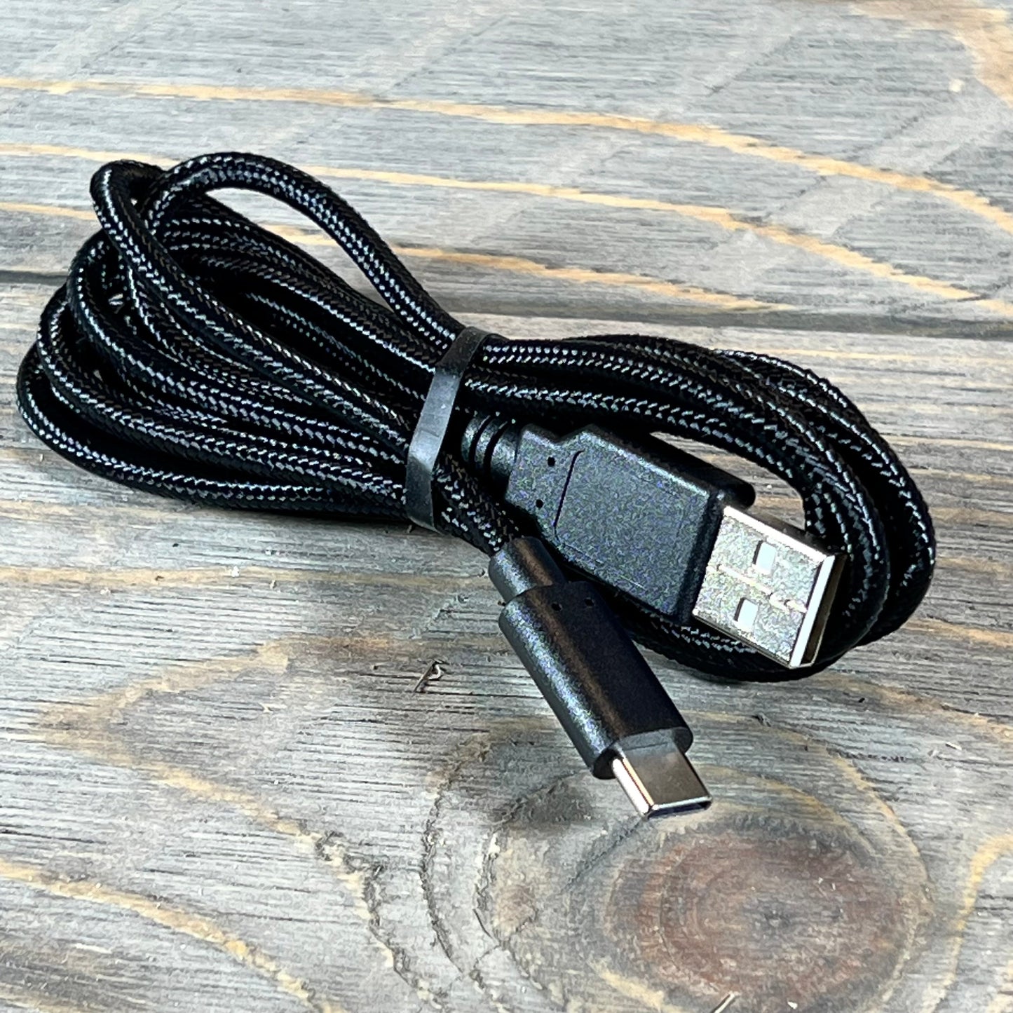 Black USB-C charging cable for EasySMX X10 Wireless Bluetooth Controller, coiled neatly on a wooden surface.