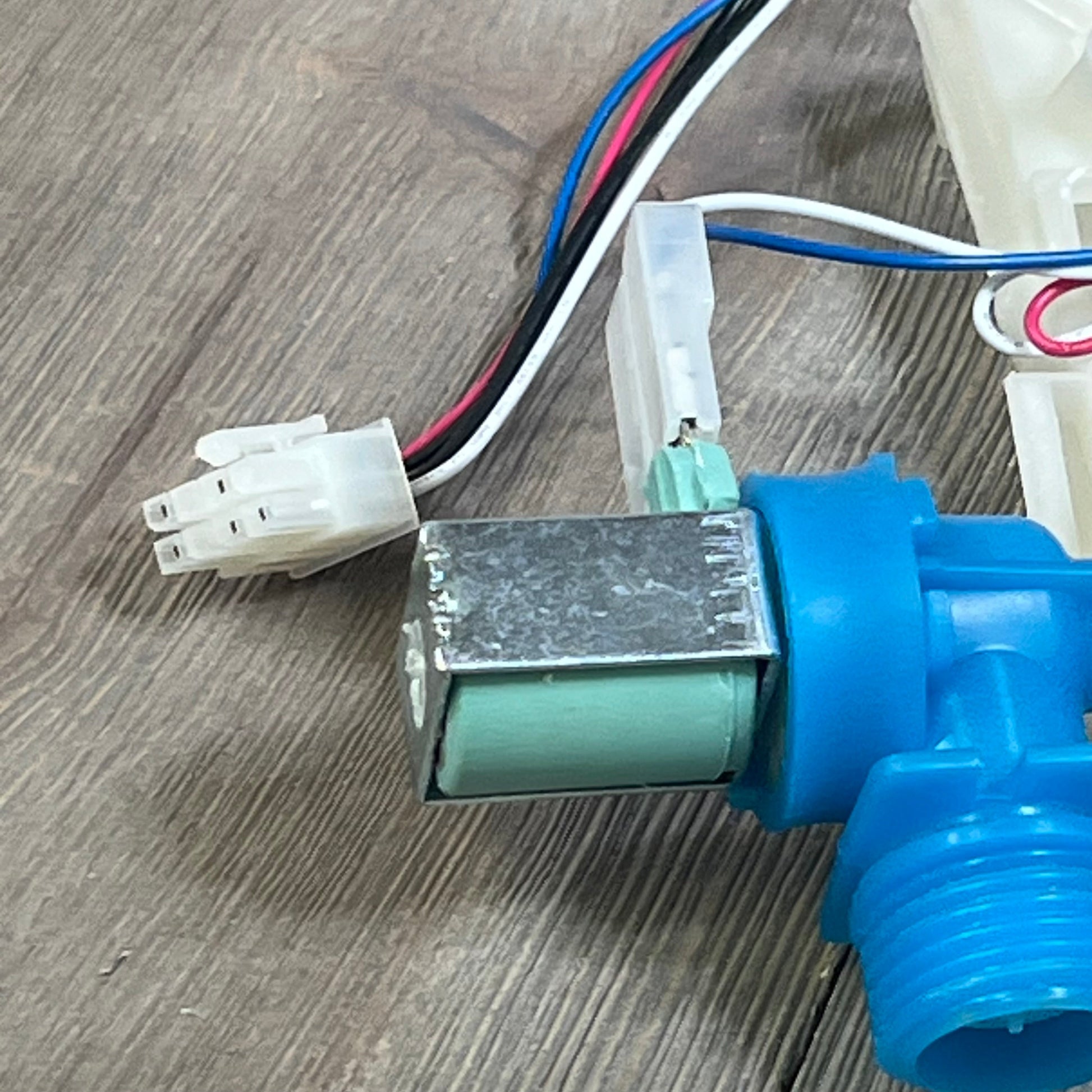 Close-up of the upgraded W10869800 washer water inlet valve, showing its wiring and blue connector for Whirlpool washers.