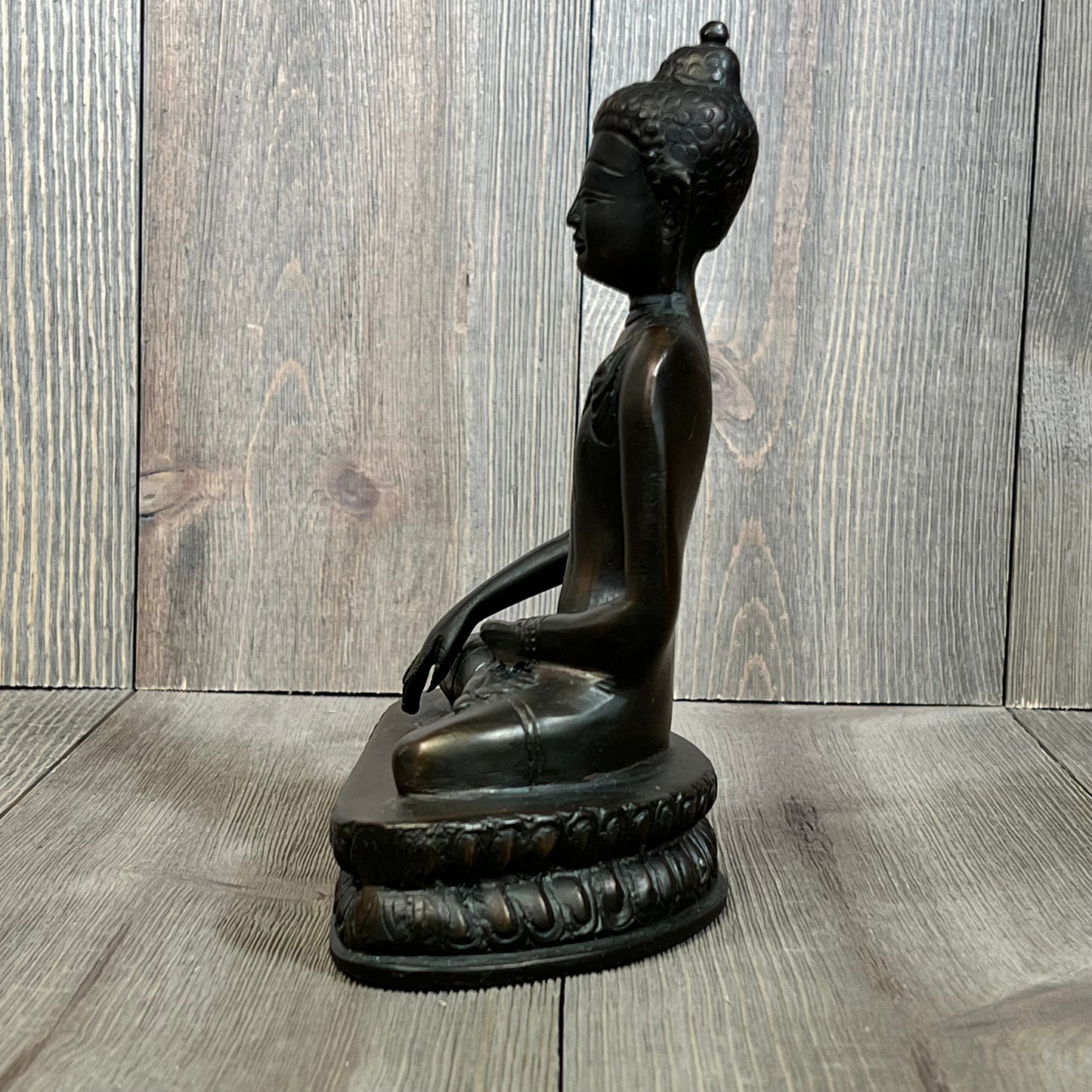 Side view of bronze Gautama Buddha statue on wooden surface, showcasing intricate details and serene expression.