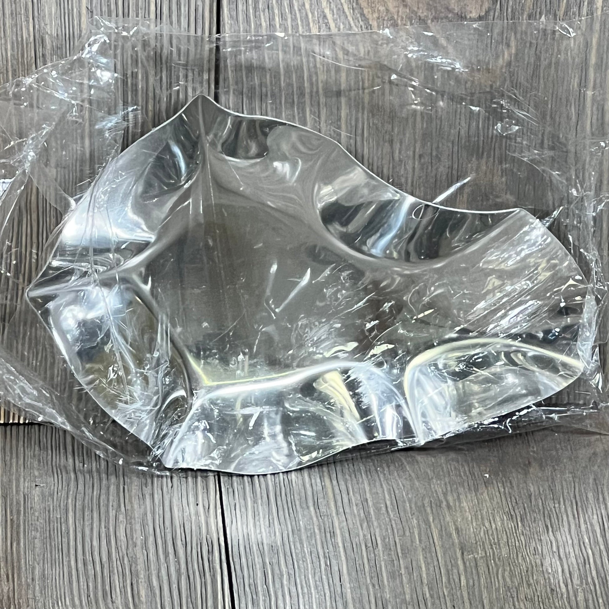 Stainless steel oyster grilling shell with clear wrap, ideal for cooking and baking, shown on a textured wooden surface.