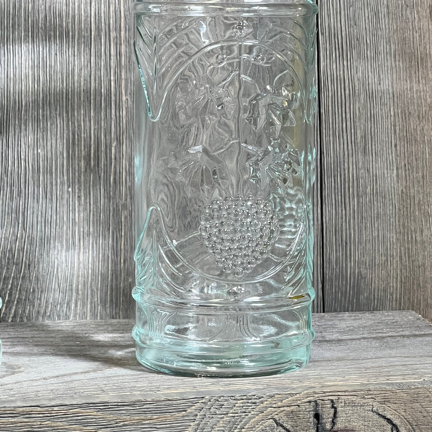Clear glass bottle with intricate grapevine design, corked top, 16oz capacity, 2.5in x 9in, perfect for decoration or storage.