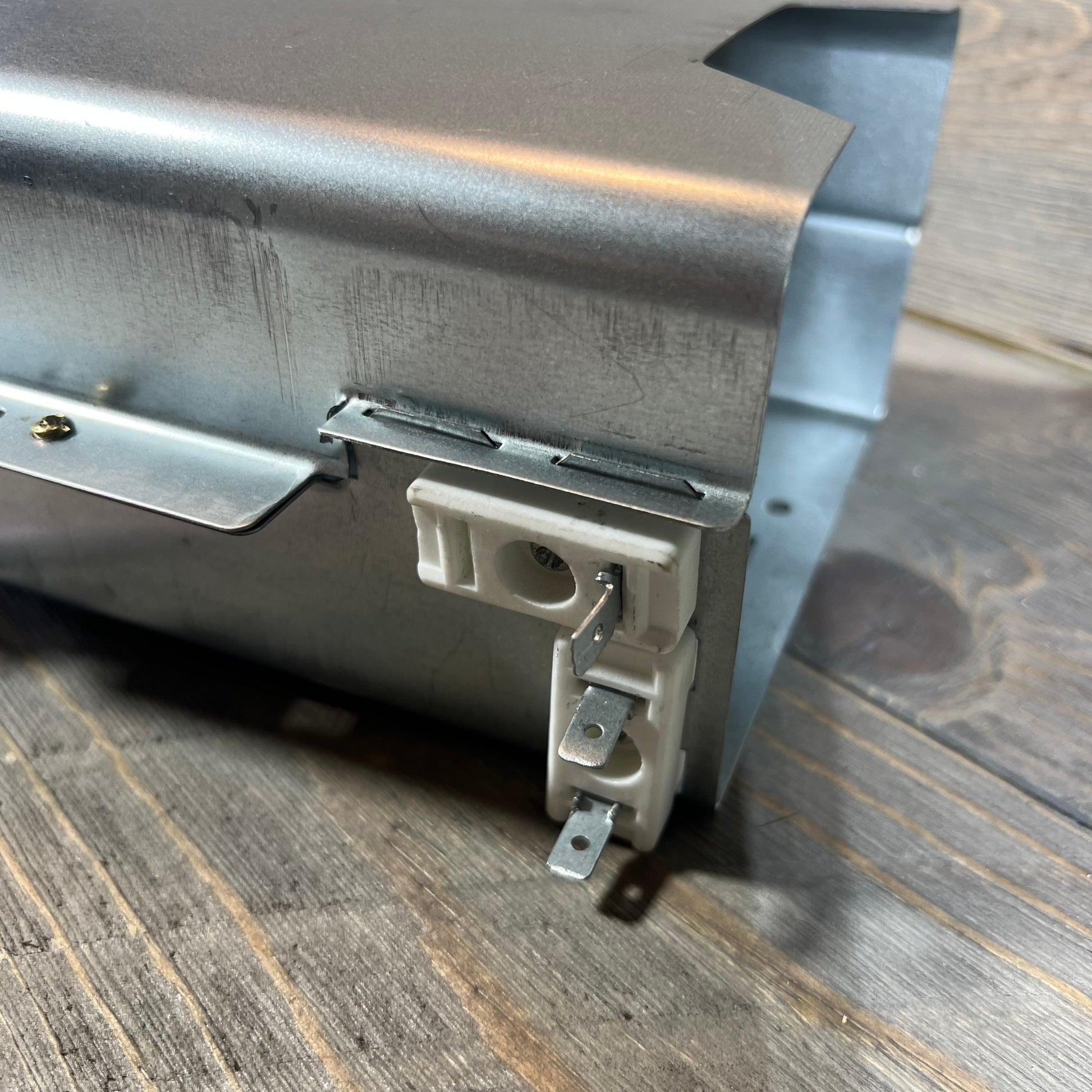 Close-up of BlueStars 5301EL1001A dryer heating element showing metal casing and connectors on wood surface.