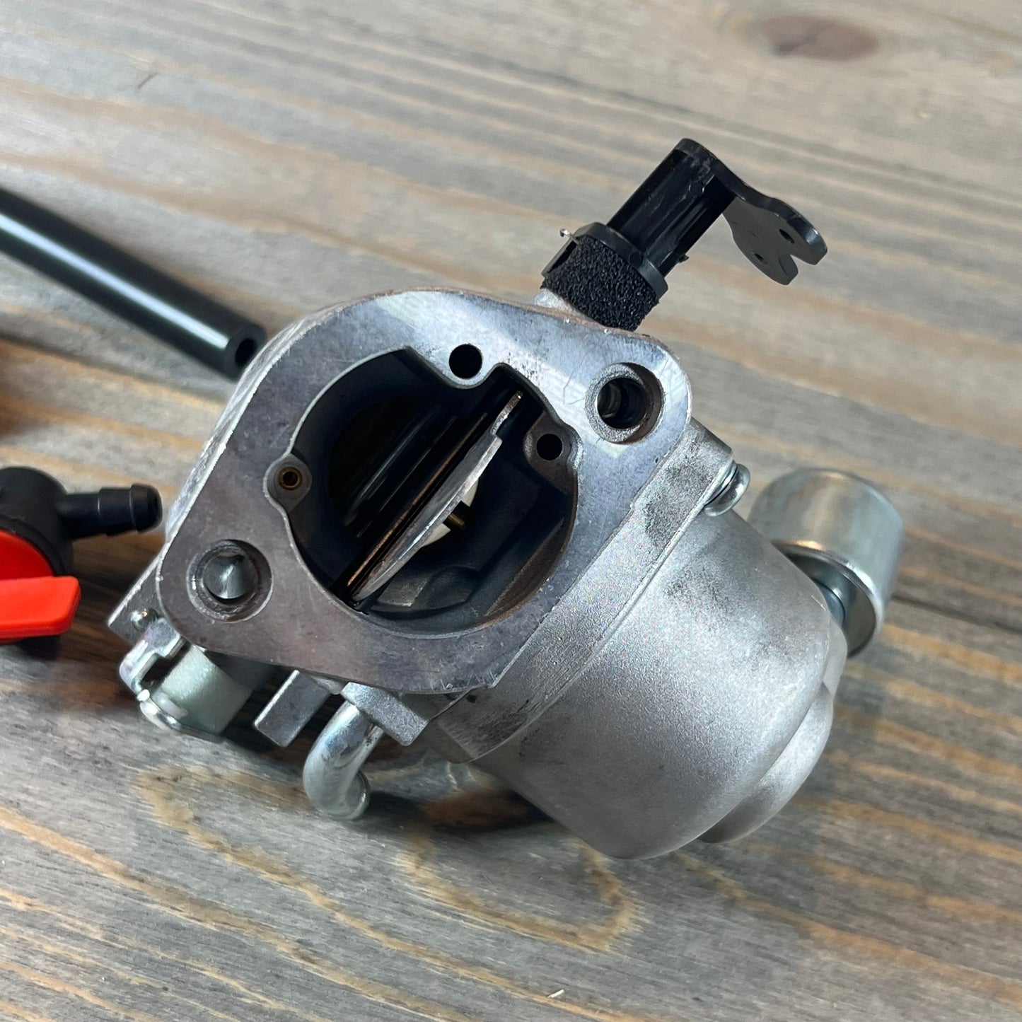 Close-up of the CARBBIA 594207 carburetor, compatible with 40N777 and 40N877 Intek engines, on a wood surface.
