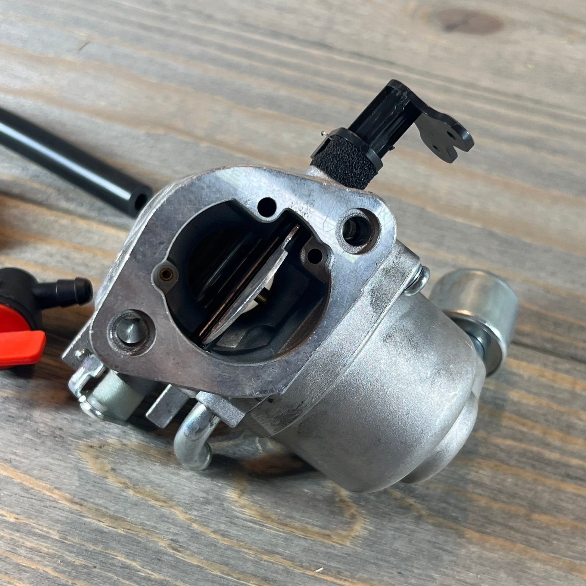 Close-up of the CARBBIA 594207 carburetor, compatible with 40N777 and 40N877 Intek engines, on a wood surface.