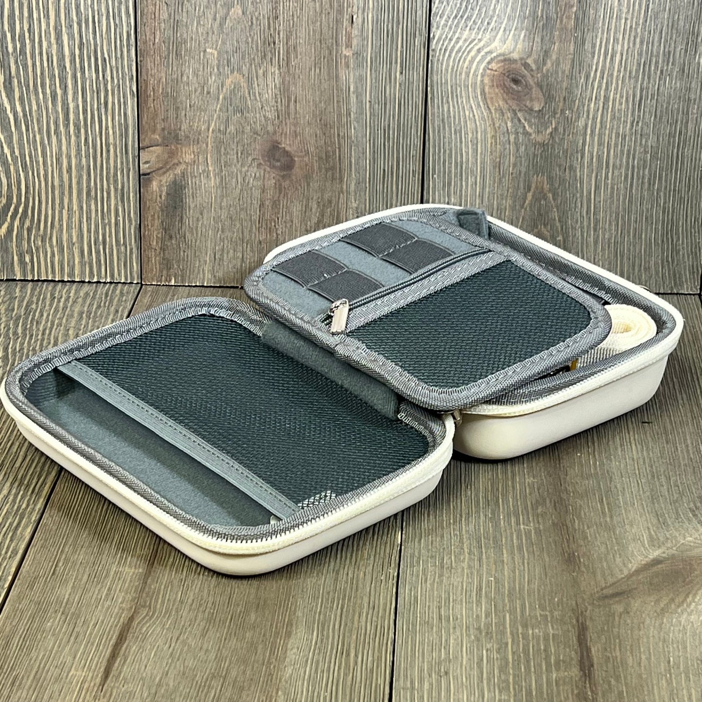 Beige K&F Concept camera case open on wooden floor, showing interior compartments and zippered mesh pocket.