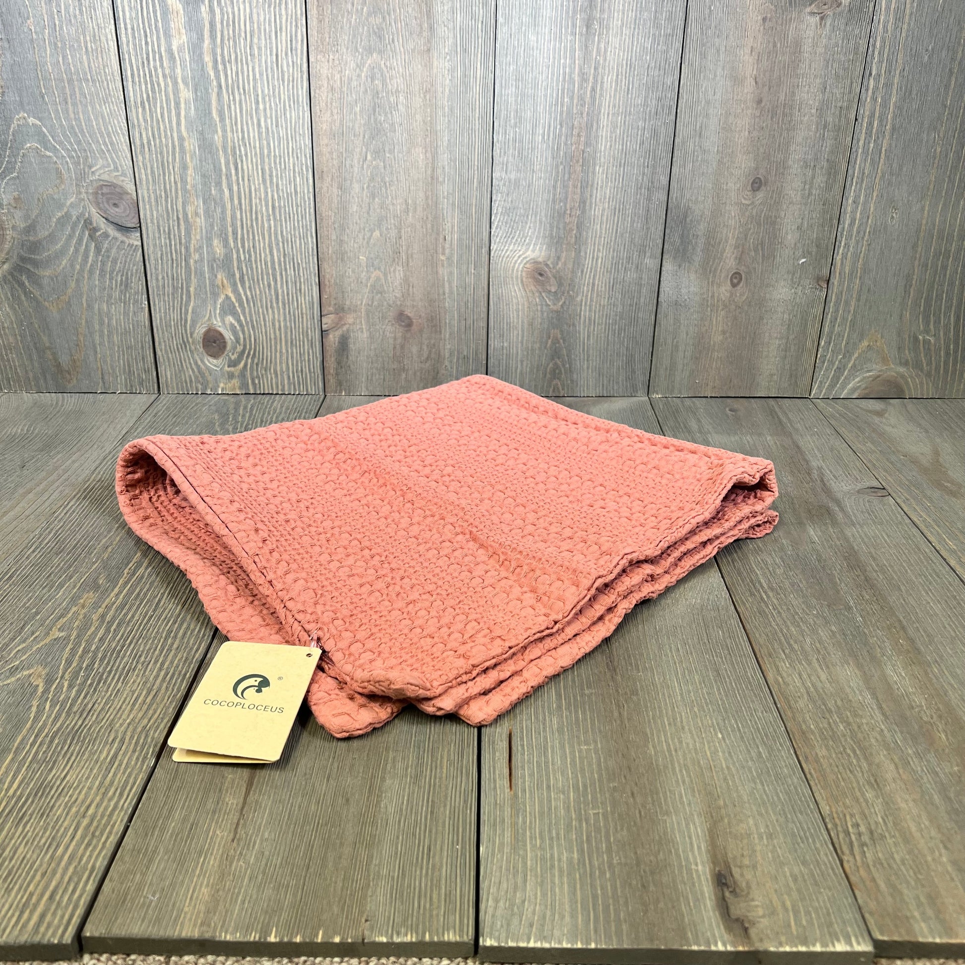 Coral pink cotton pillow cover folded on a wooden surface, ideal for boho decor, 24x24 inch size by COCOPLOCEUS.