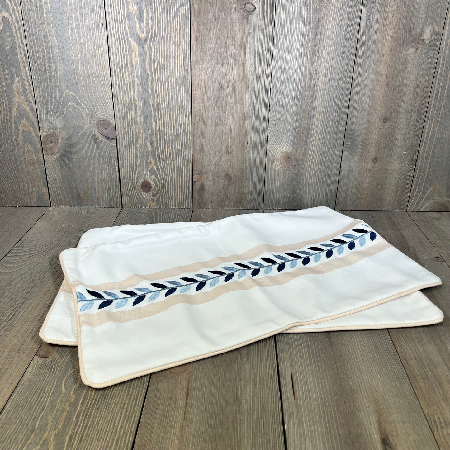 Tan lumbar pillow cover with blue leaf embroidery, perfect for patio decor, water-repellent fabric for outdoor use.