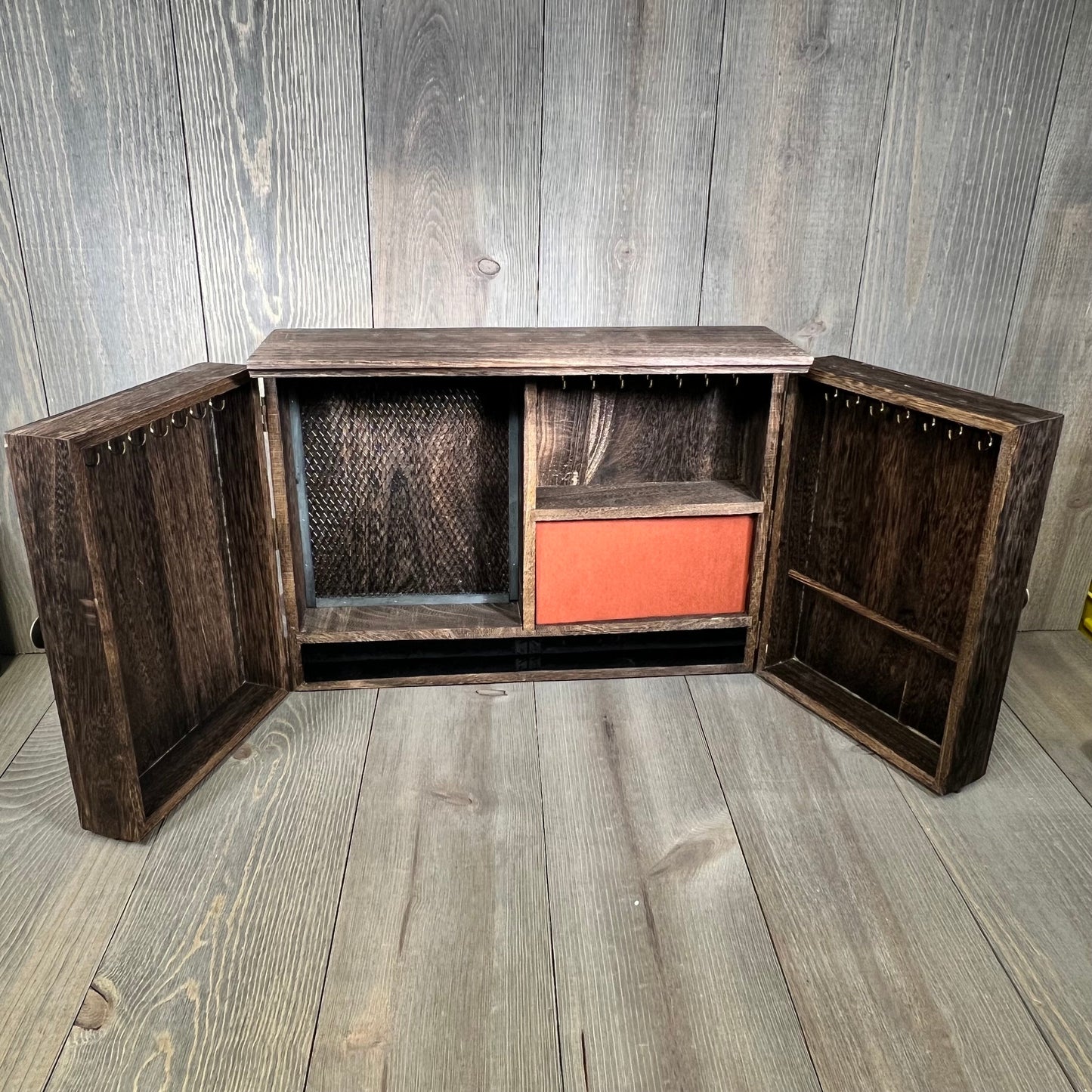 Rustic wooden jewelry organizer with open barn door design, featuring hooks and compartments for necklaces and rings.