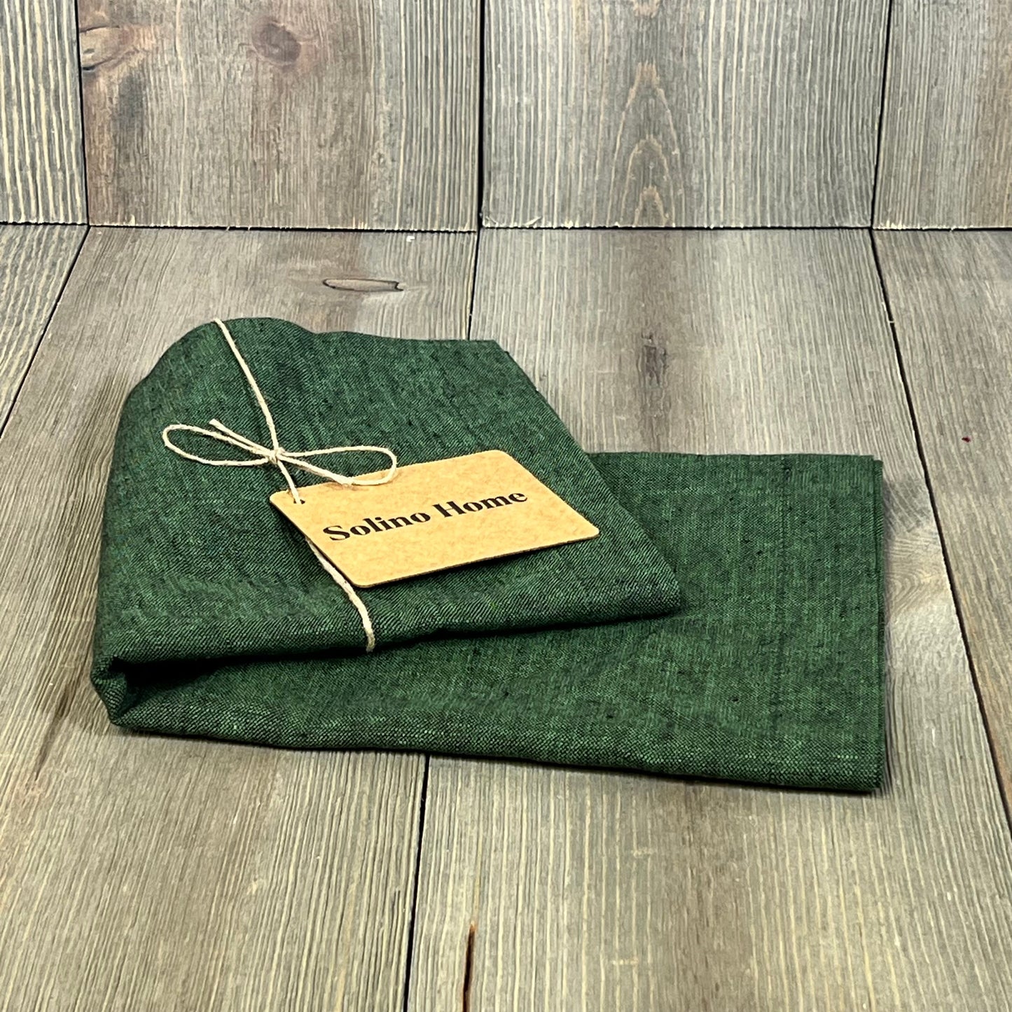 Forest Green Linen Table Runner by Solino Home, 14 x 36 inches, elegantly folded with a rustic tag on wood background.