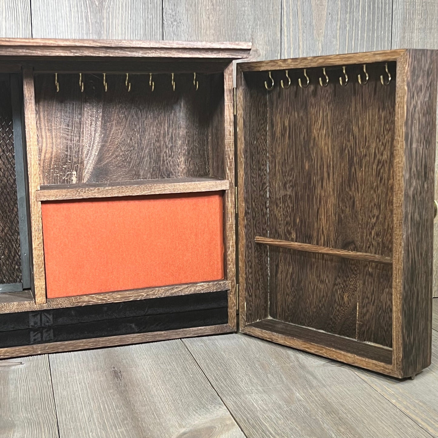 Rustic wooden barn door jewelry organizer open, showcasing hooks and compartments for necklaces and earrings.