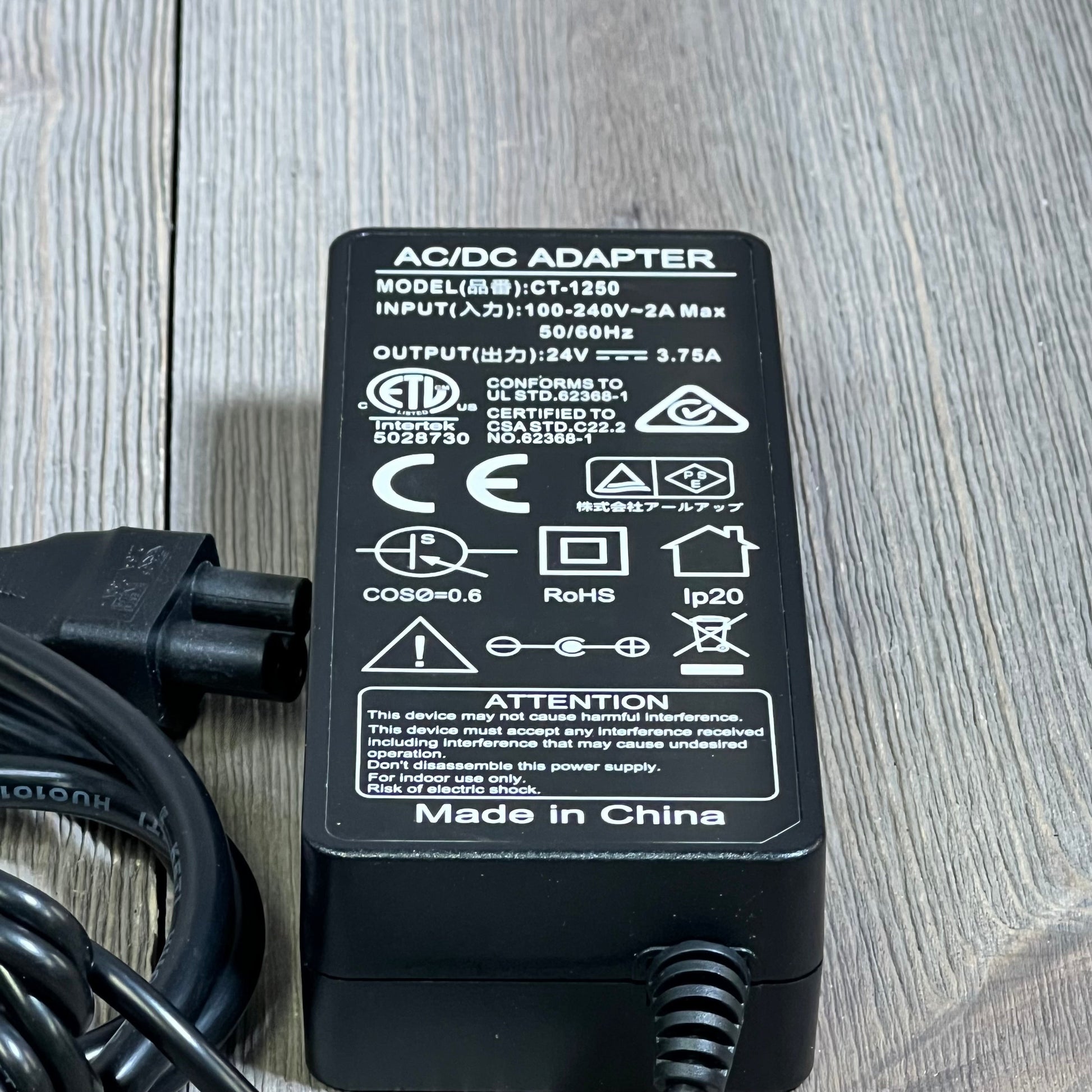 24V 90W AC adapter for Jackery portable power station, showing safety certifications and specifications on wooden surface.