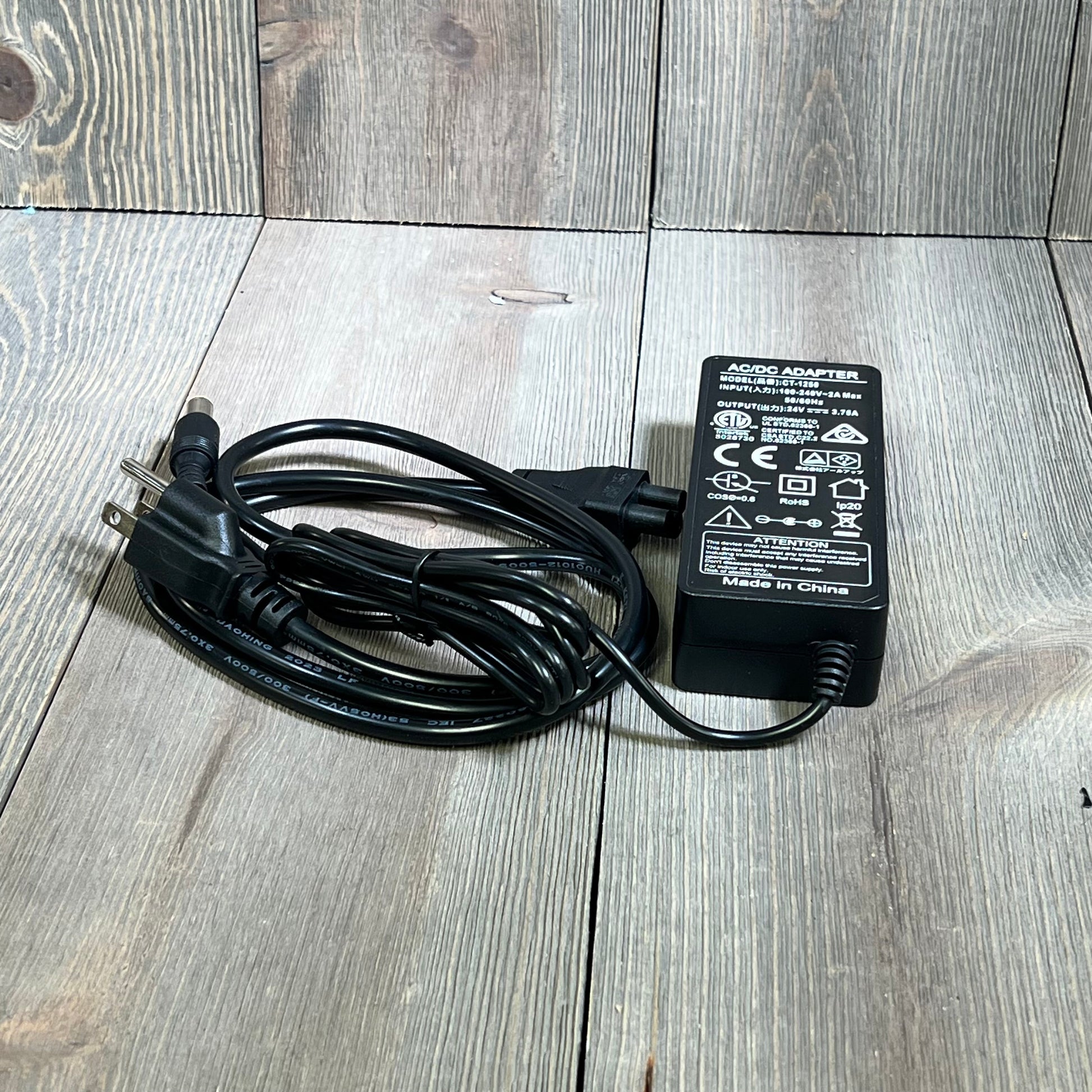 Black 24V 90W AC adapter for Jackery portable power stations, with power cord, resting on a wooden surface.