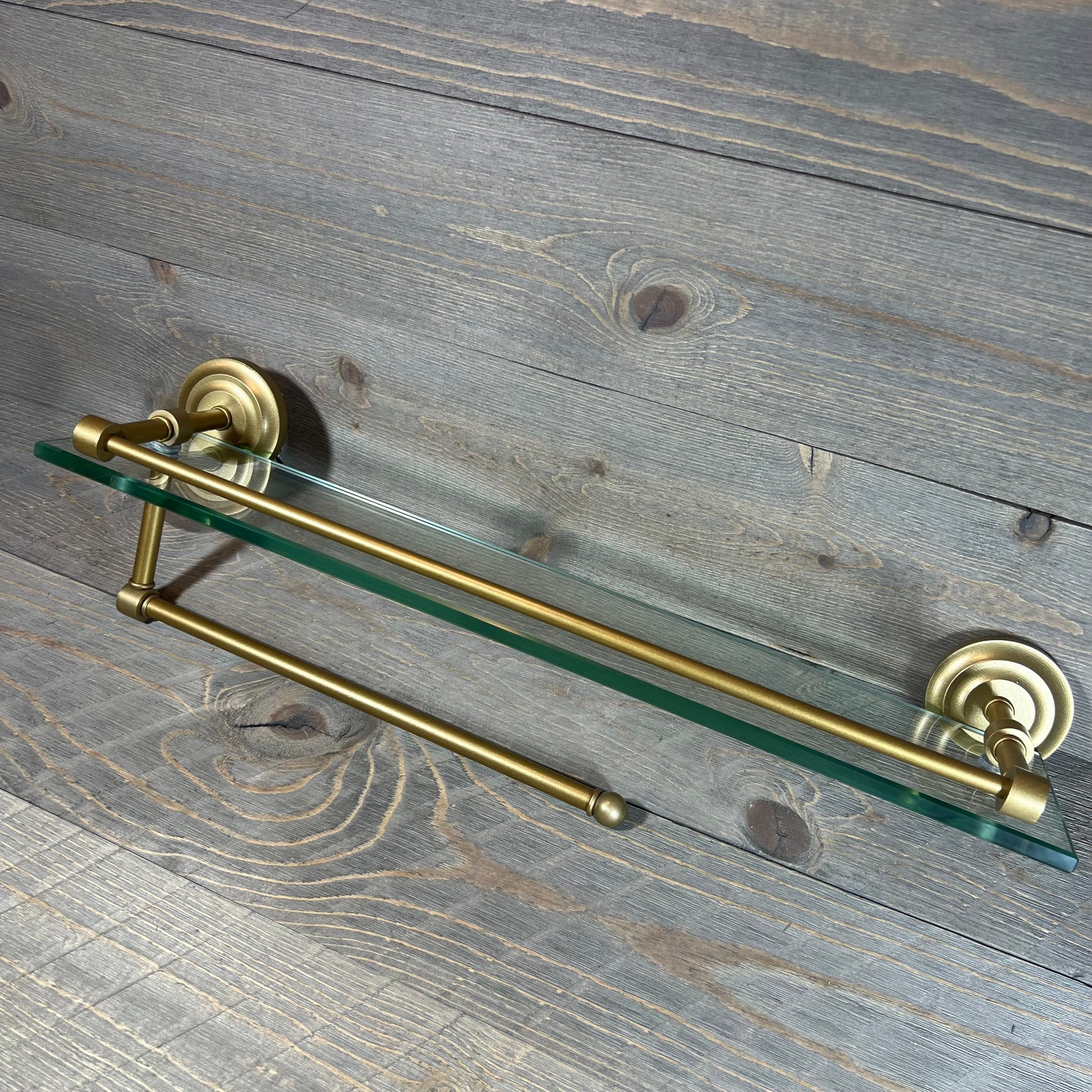 Elegant brass paper towel holder with 22" glass shelf on rustic wood background.