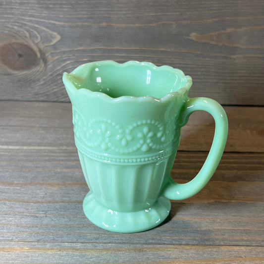 Elegant jade creamer with intricate embossed detailing on a wooden background.