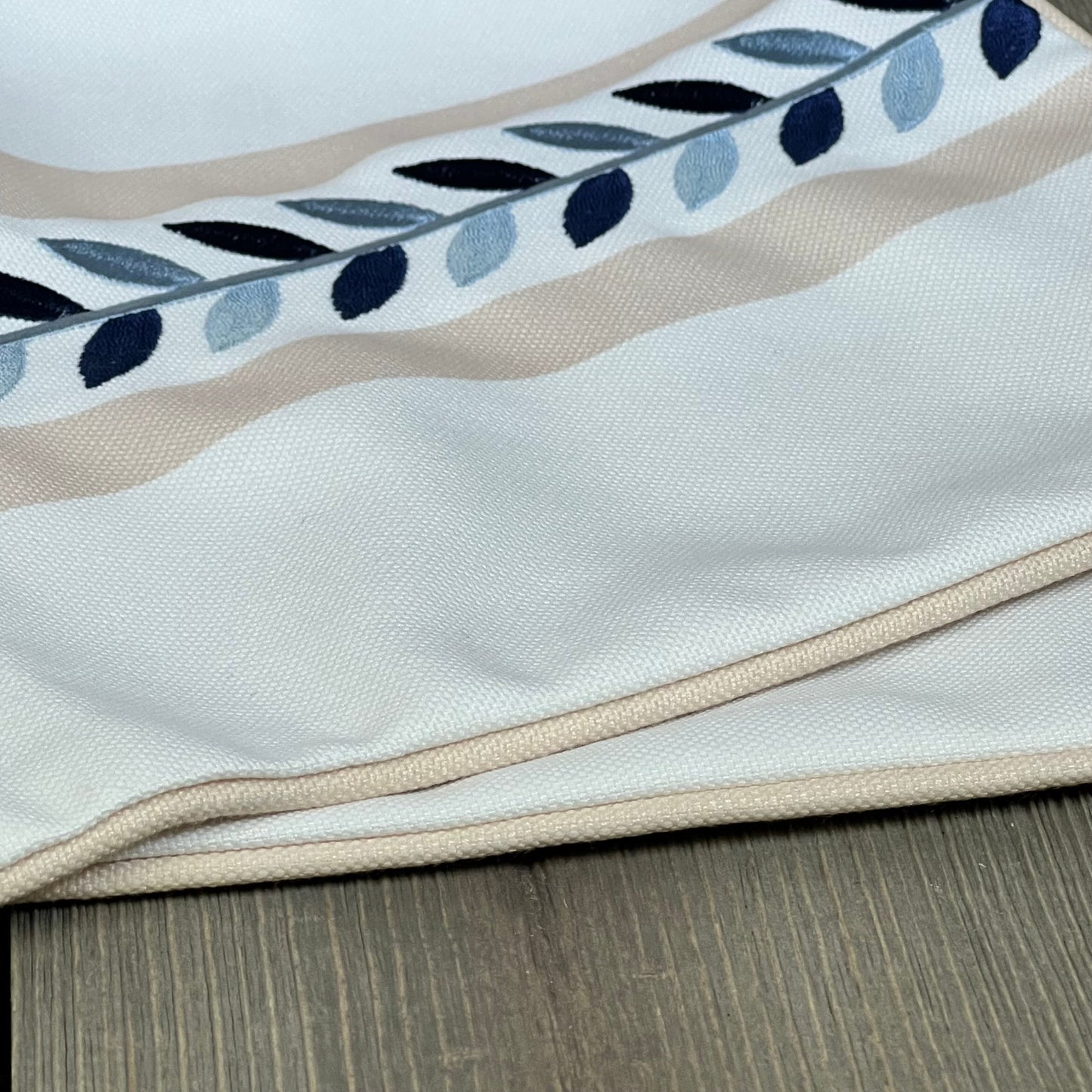 Coastal lumbar pillow cover with tan piping and embroidered leaf design, perfect for patios and couches. Water-repellent fabric.