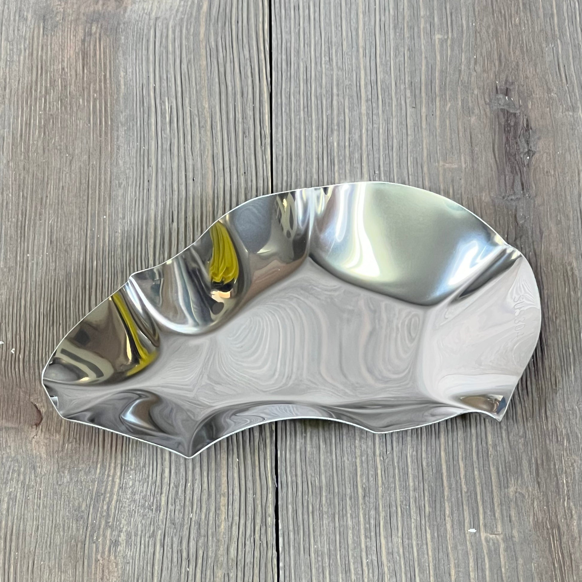Stainless steel oyster grilling shell on wooden surface, ideal for cooking and baking seafood dishes.