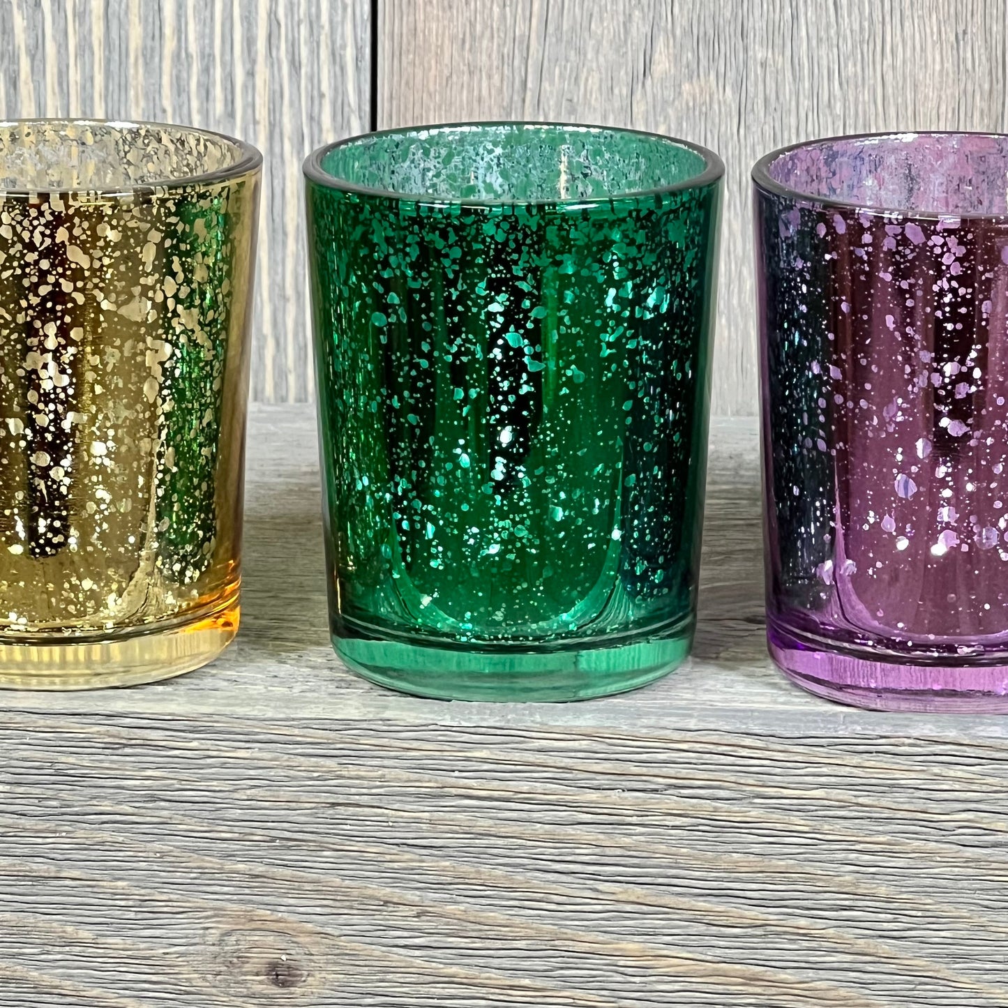 Assorted jewel tone mercury glass votive candle holders in deep gold, green, and purple hues, perfect for elegant decor.